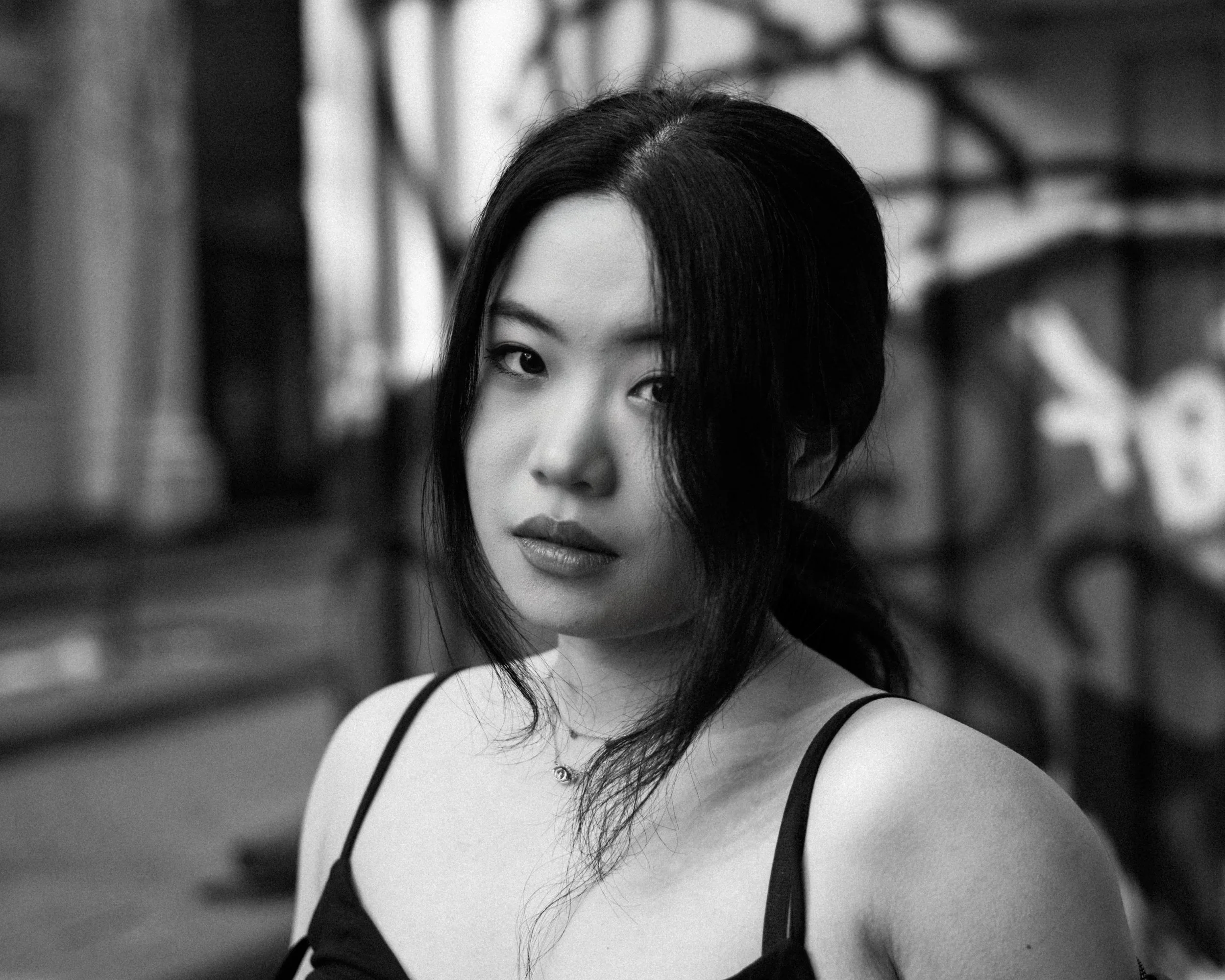 On the cobbled streets of Soho in New York City, a woman is looking into the camera with a sense of sorrow. Behind her, graffiti and City store fronts are visible.