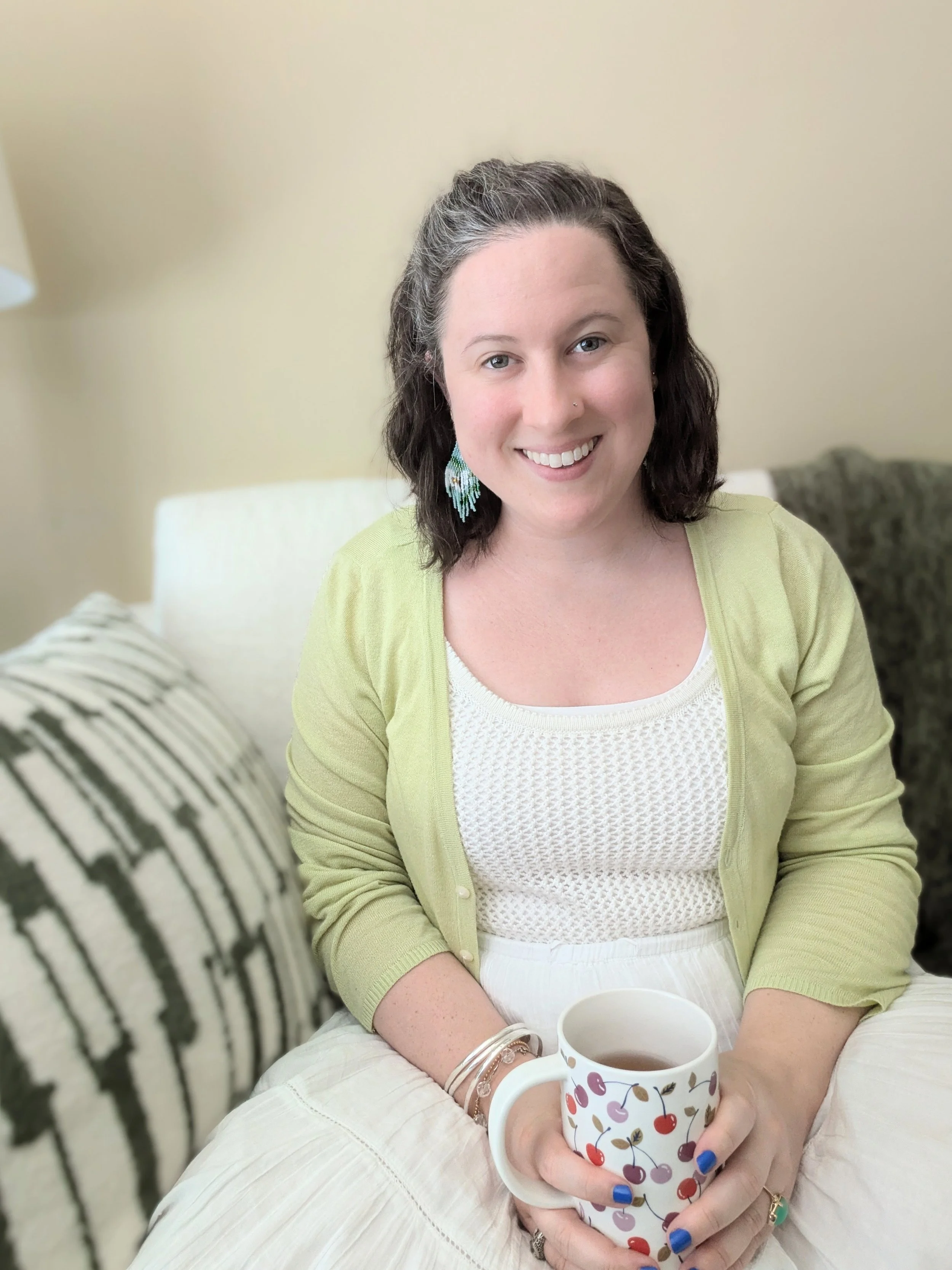image of woman smiling sitting on a couch and holding a cup of tea