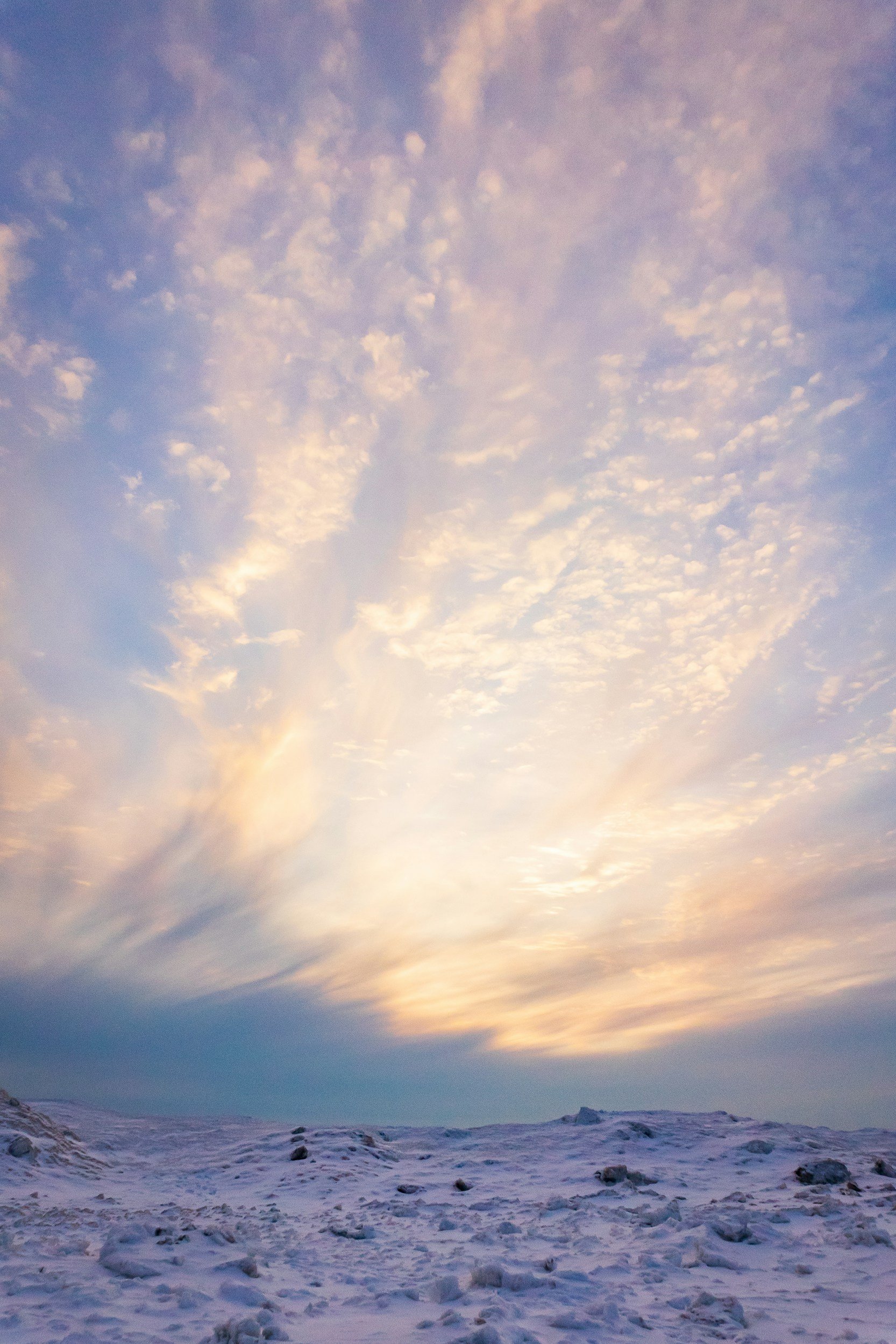 Snow-covered landscape with a cloudy sky during sunset or sunrise.