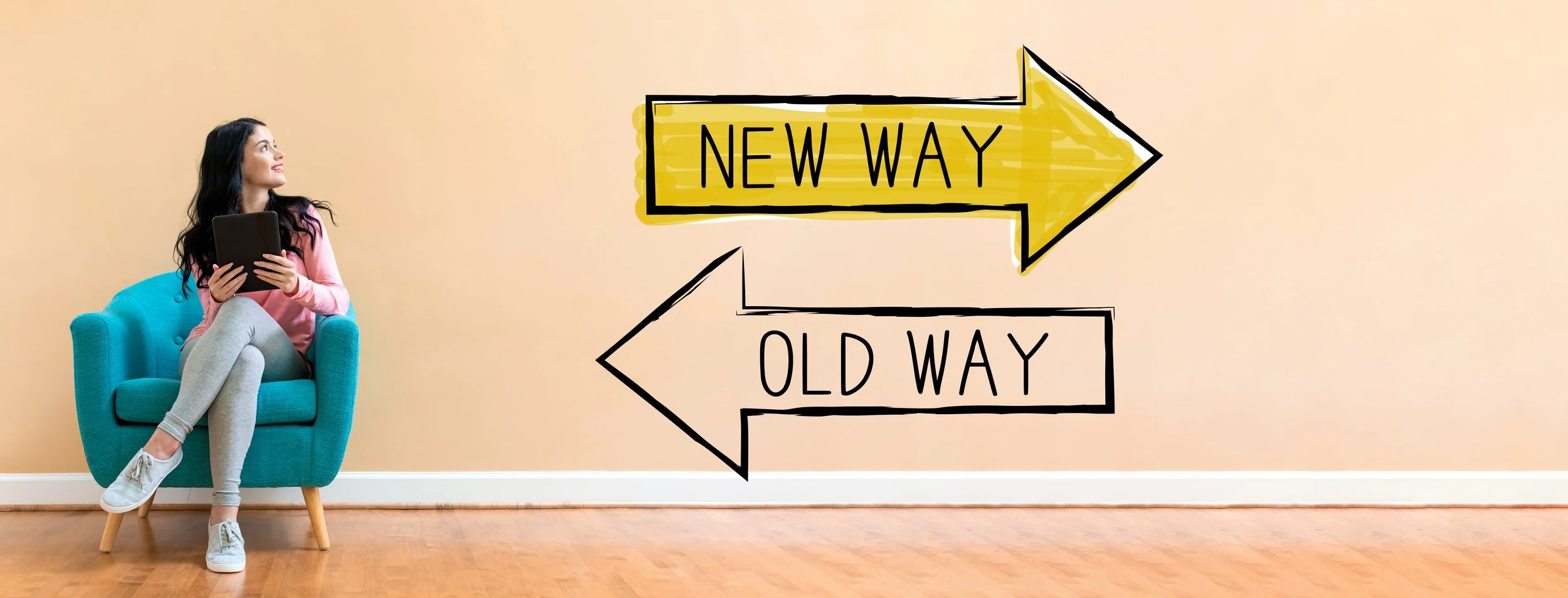 A woman sitting in a teal armchair holding a tablet, looking to her left. Two directional signs on the wall behind her read 'New Way' pointing to the right and 'Old Way' pointing to the left.