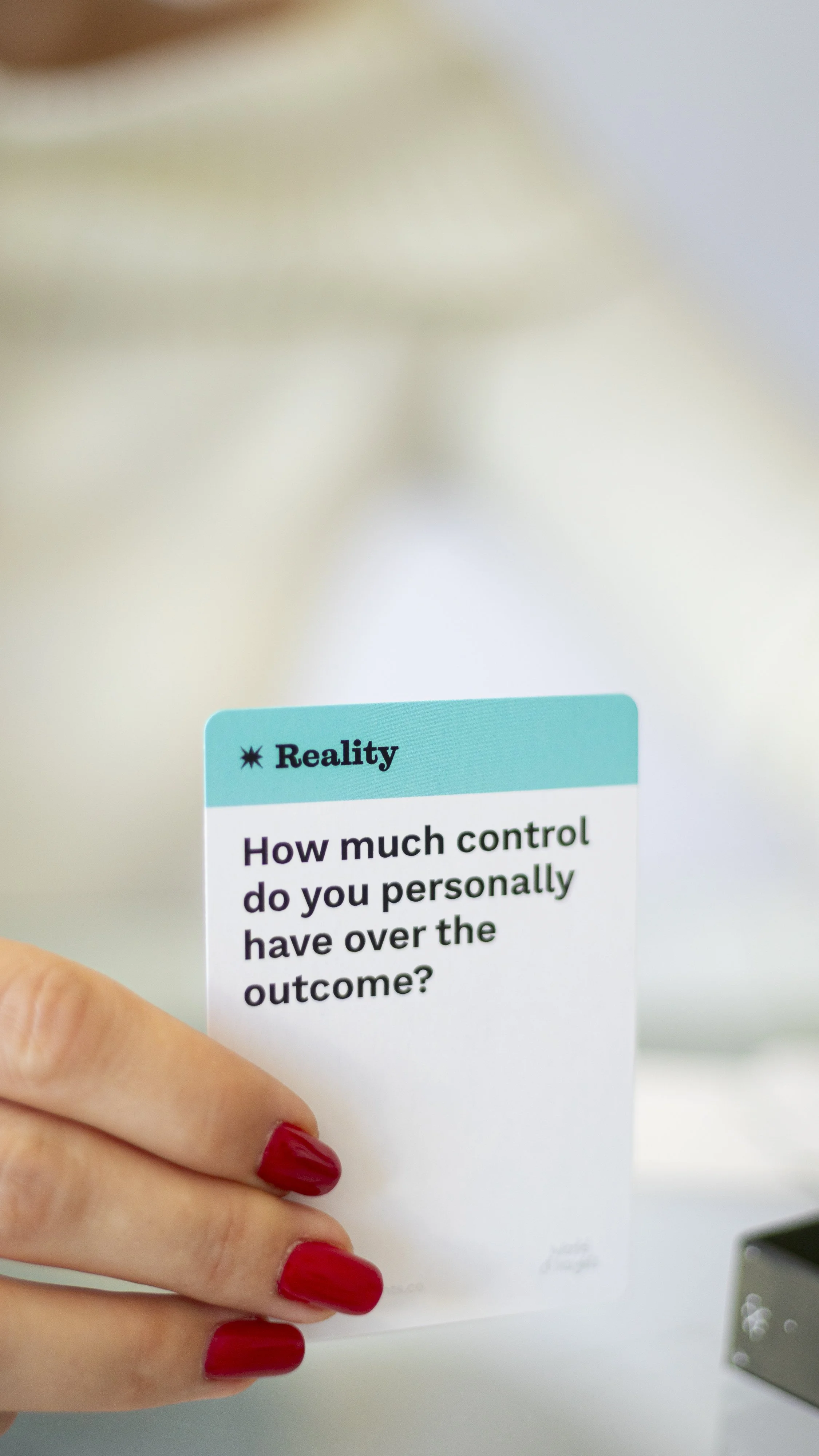 Close-up of a hand with red painted nails holding a card that reads, 'ReaLity: How much control do you personally have over the outcome?'