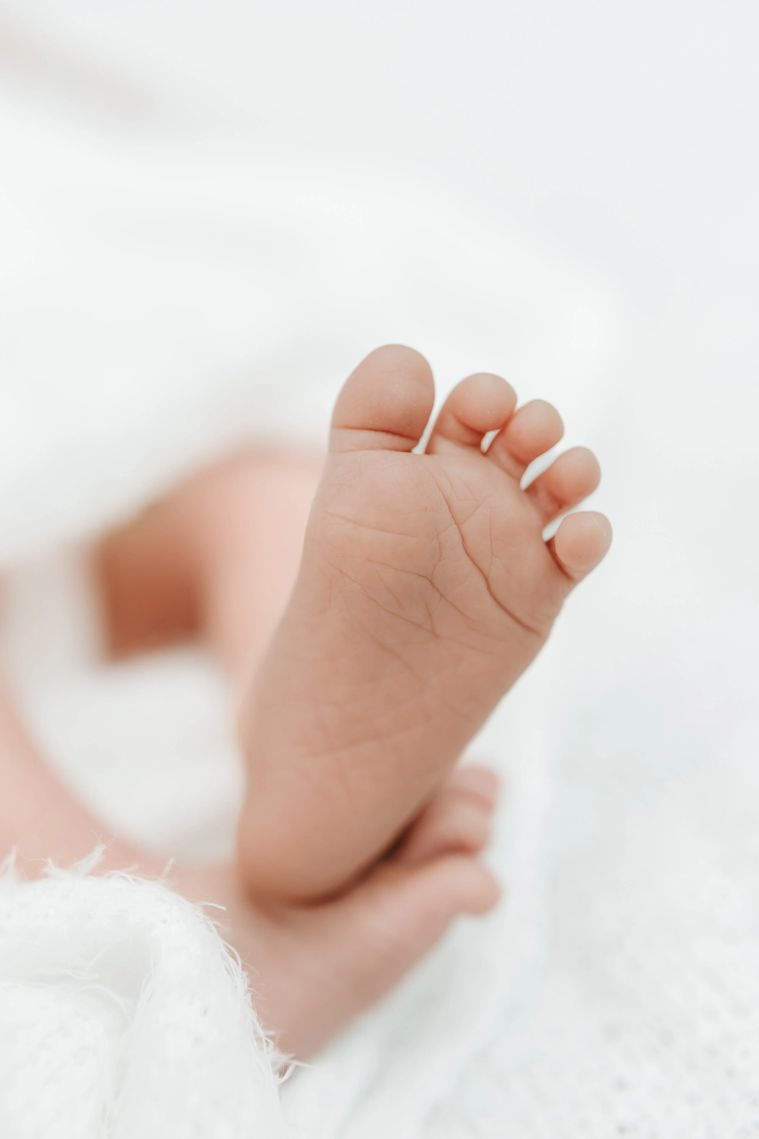 Close-up of a baby's foot with tiny toes, resting on a soft white surface.