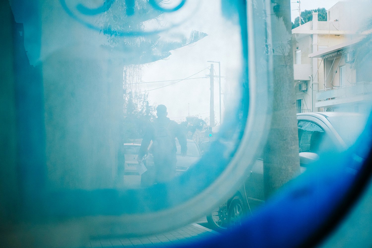 Reflexion eines Mannes mit kleinen Papieren im Fenster einer blauen Tür auf einer Stadtstraße mit Autos und Gebäuden.