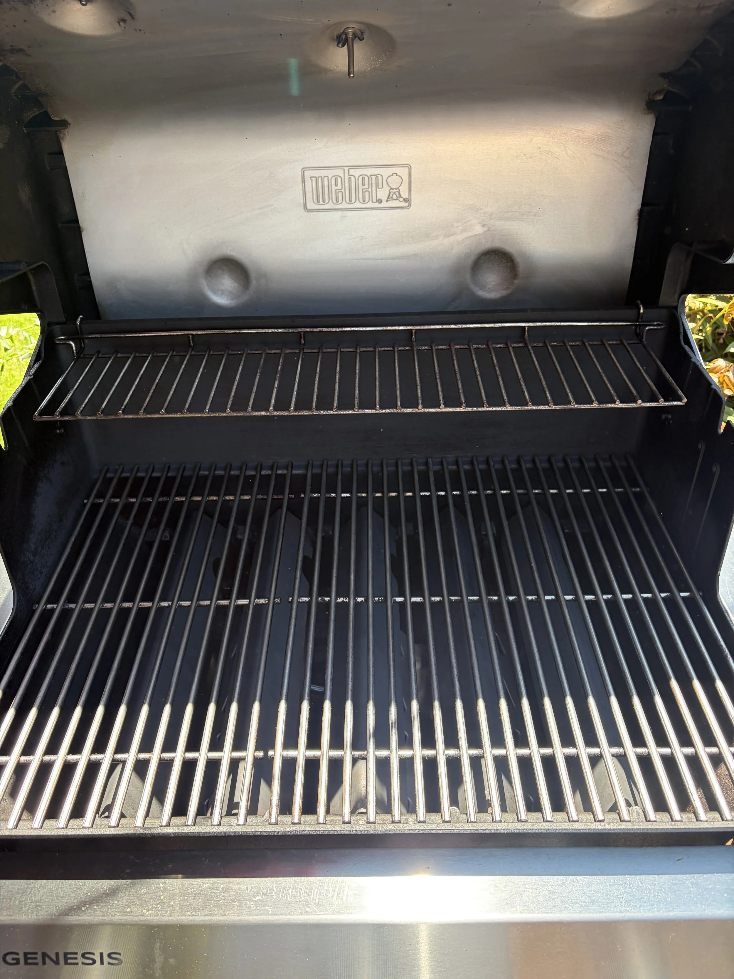 An empty stainless steel Genesis gas barbecue grill with a closed grill lid, showing a rack inside for cooking.