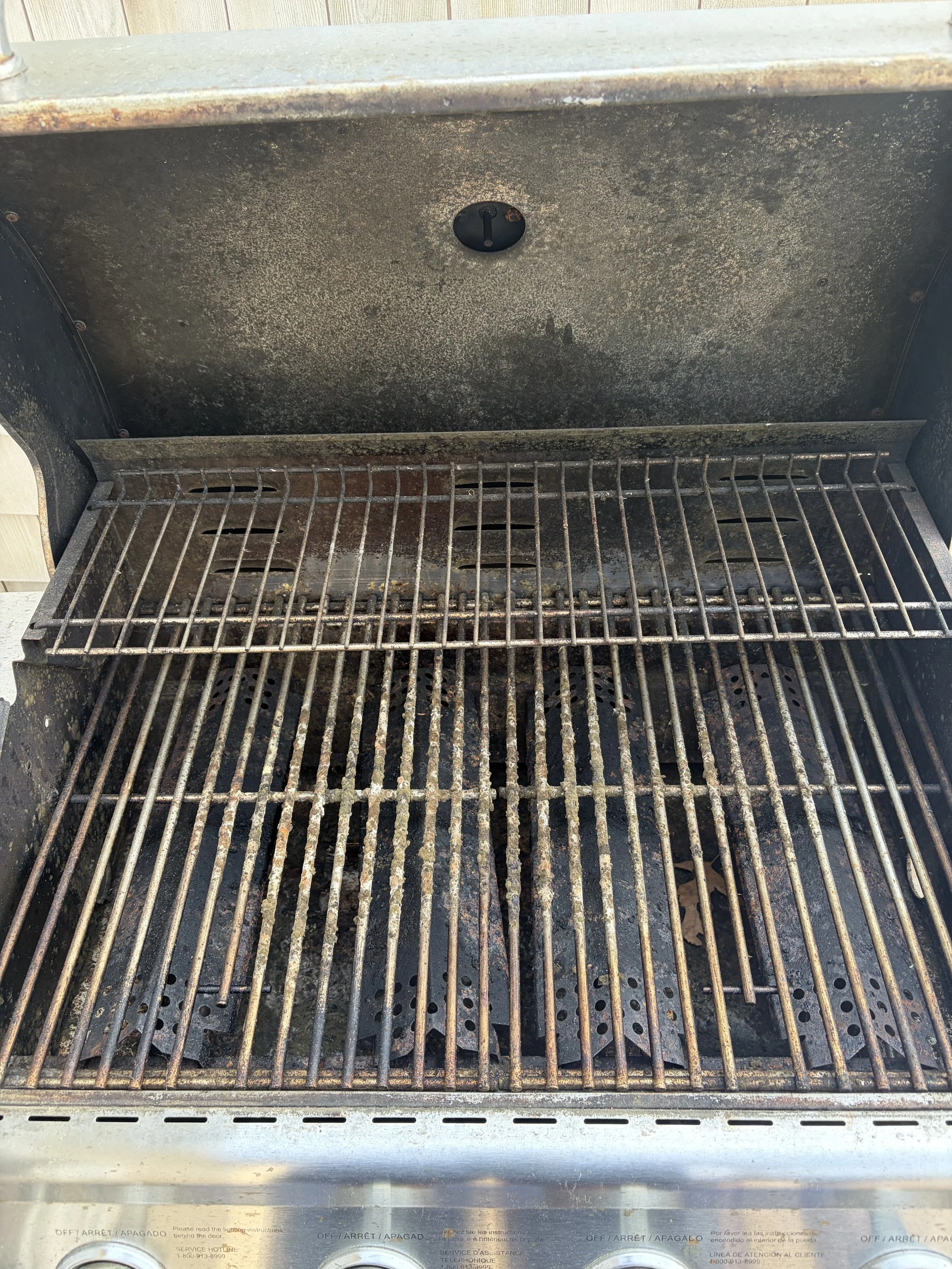 Inside view of a rusty, dirty indoor grill with metal grates and a black cover switch on the back wall.