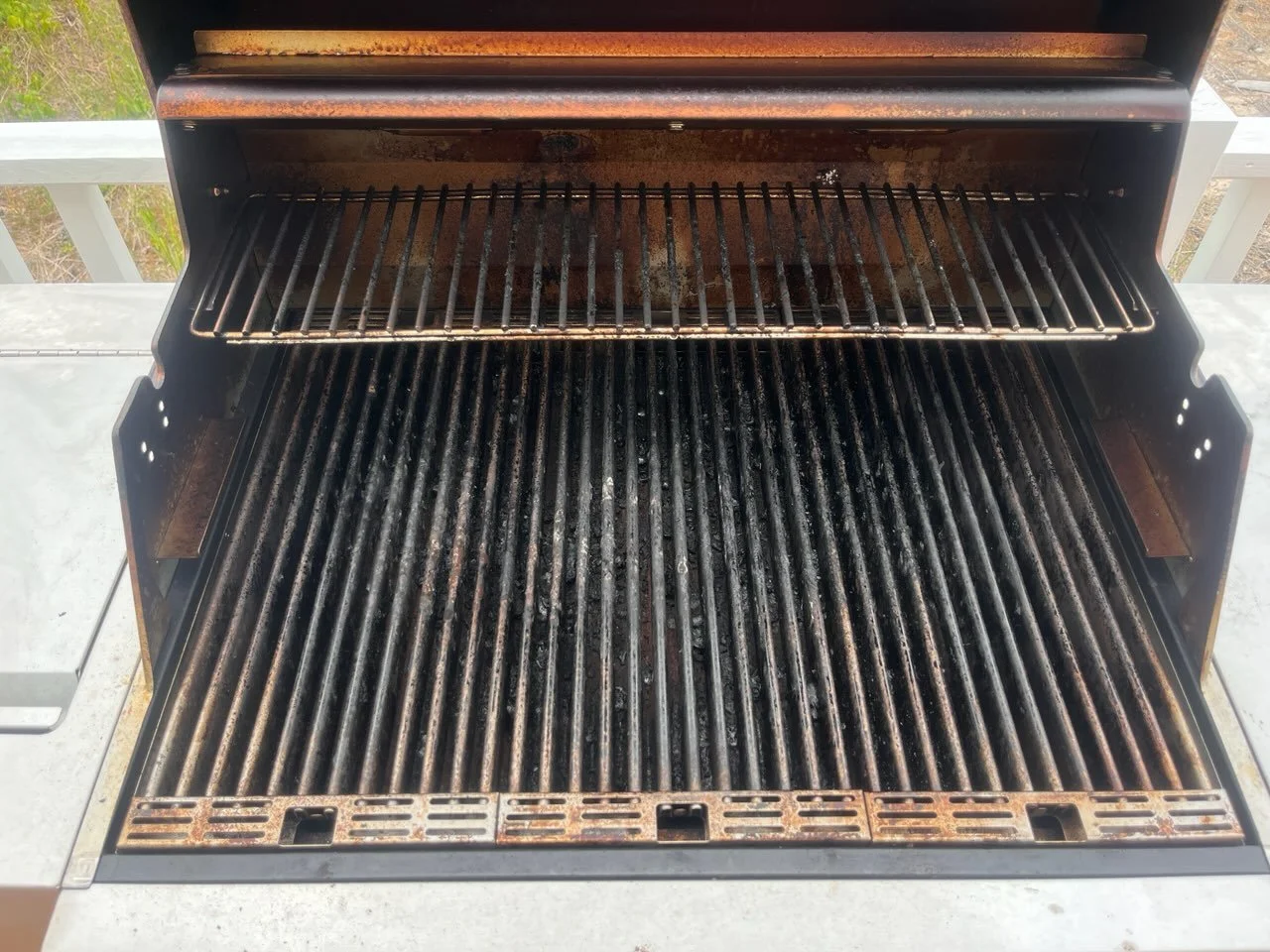 The inside of a used barbeque grill with no food, showing blackened grates and rust on the upper rack.
