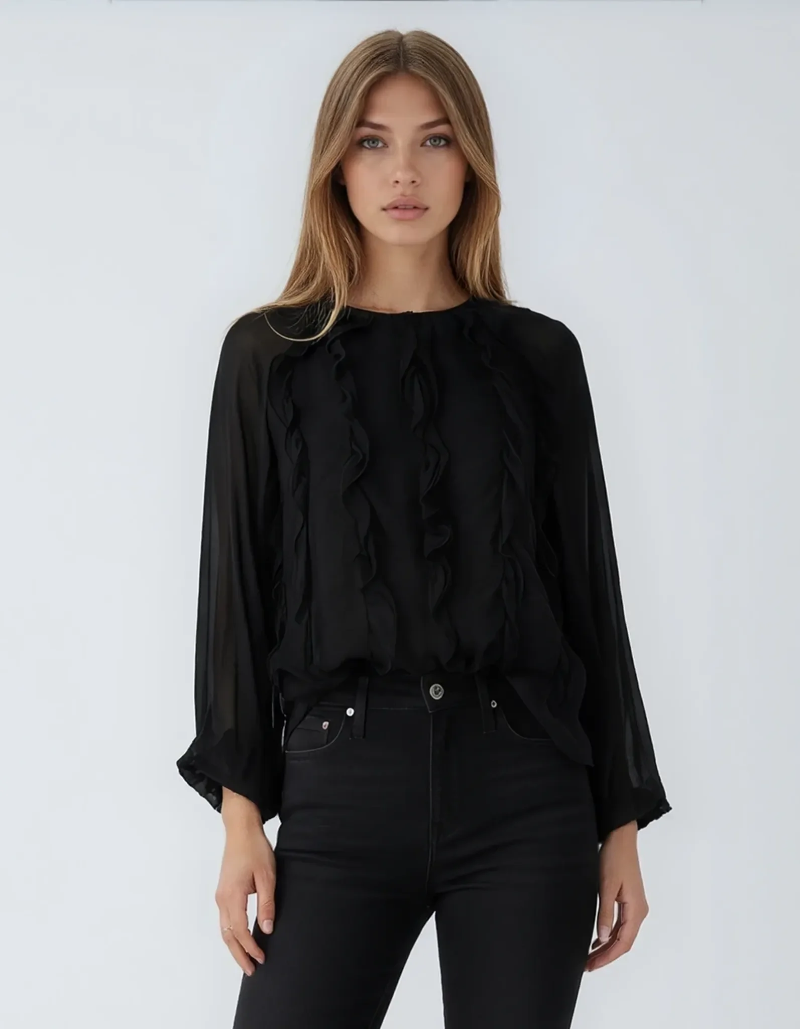 Model trägt die schwarze MAE Volantbluse kombiniert mit einer schwarzen Jeans – eleganter All-Black-Look.