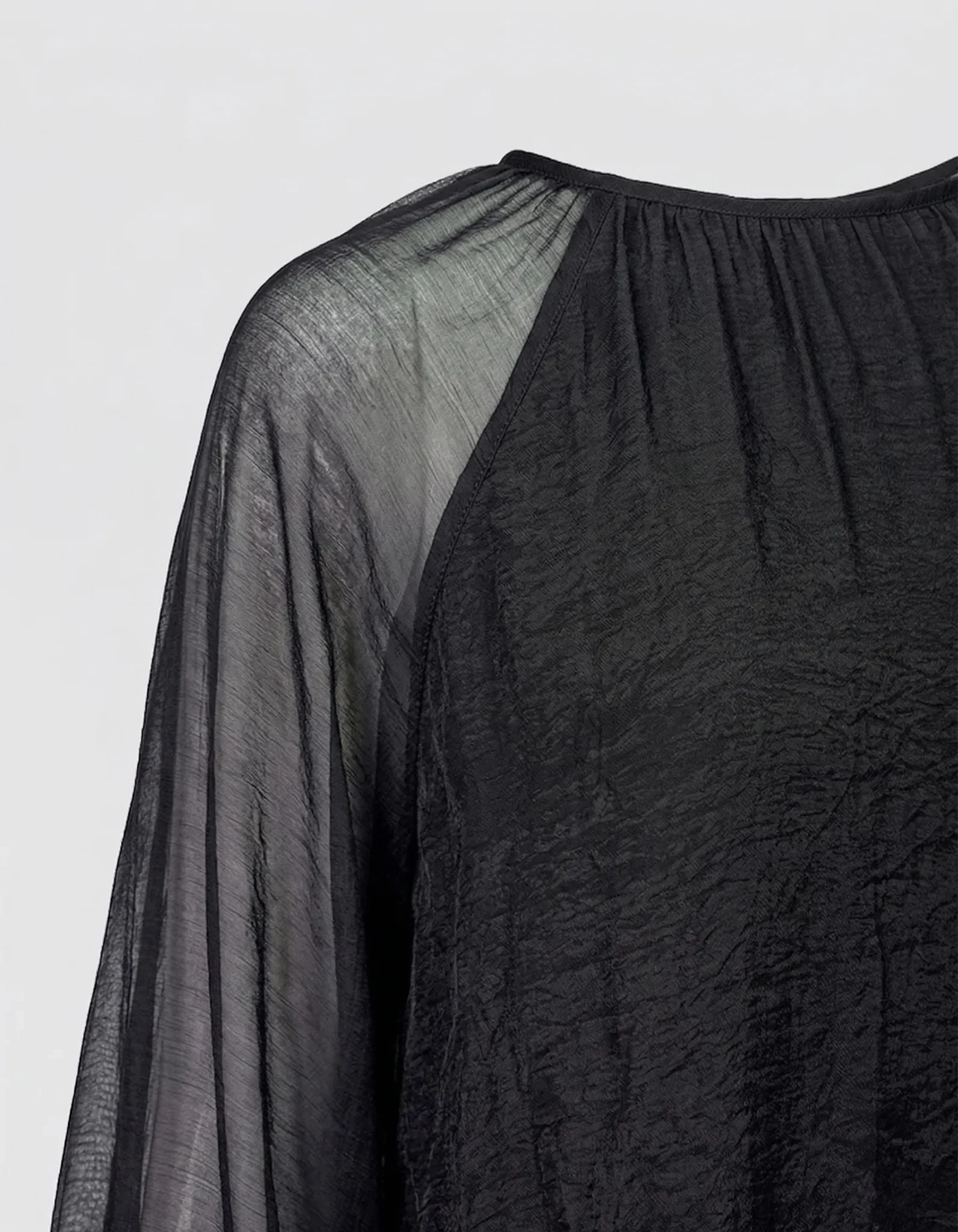 Detailansicht der MAE Bluse: Feine Chiffon-Struktur in Tiefschwarz mit gerafftem Rundhalsausschnitt.