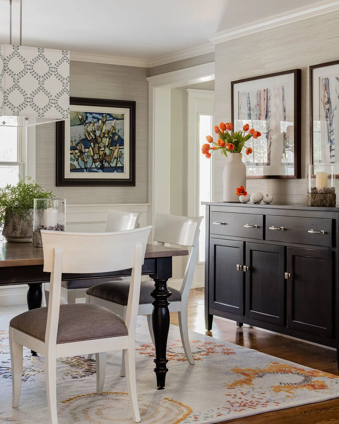Transitional dining room with grey grasscloth wallcovering, dark pedestal table, white painted dining chairs, and black buffet — full service interior design in Essex County MA by Sacris Design
