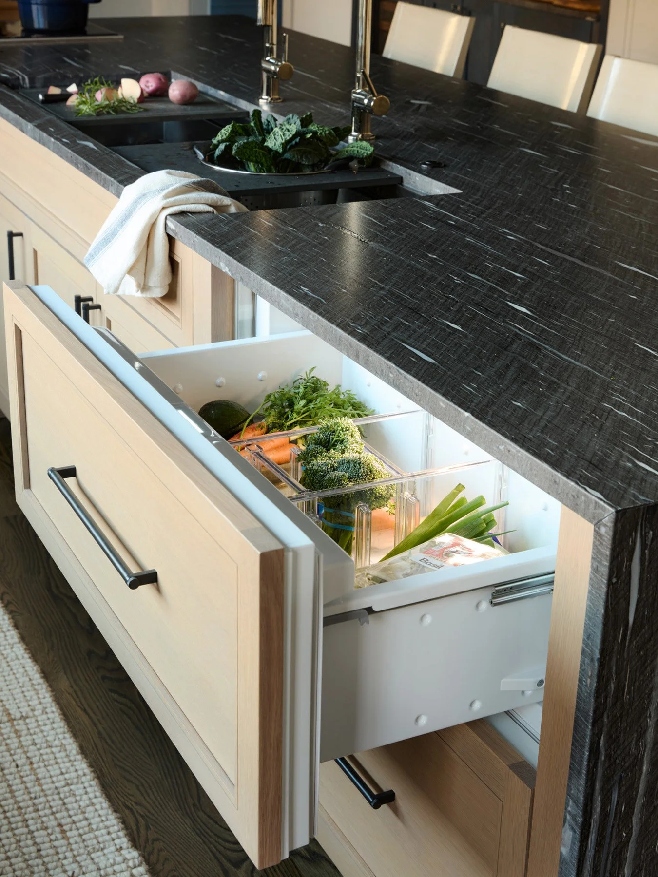 SACRIS island with integrated Sub-Zero refrigeration drawers in white oak cabinetry beneath leathered black stone, North Andover Massachusetts