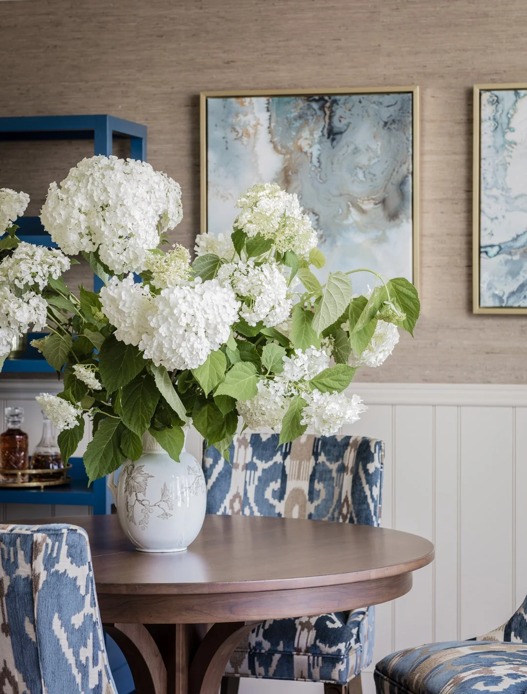 Dining room detail with white hydrangea arrangement, blue ikat upholstered chairs, and grasscloth wallcovering — traditional interior design on the North Shore of Massachusetts by SACRIS