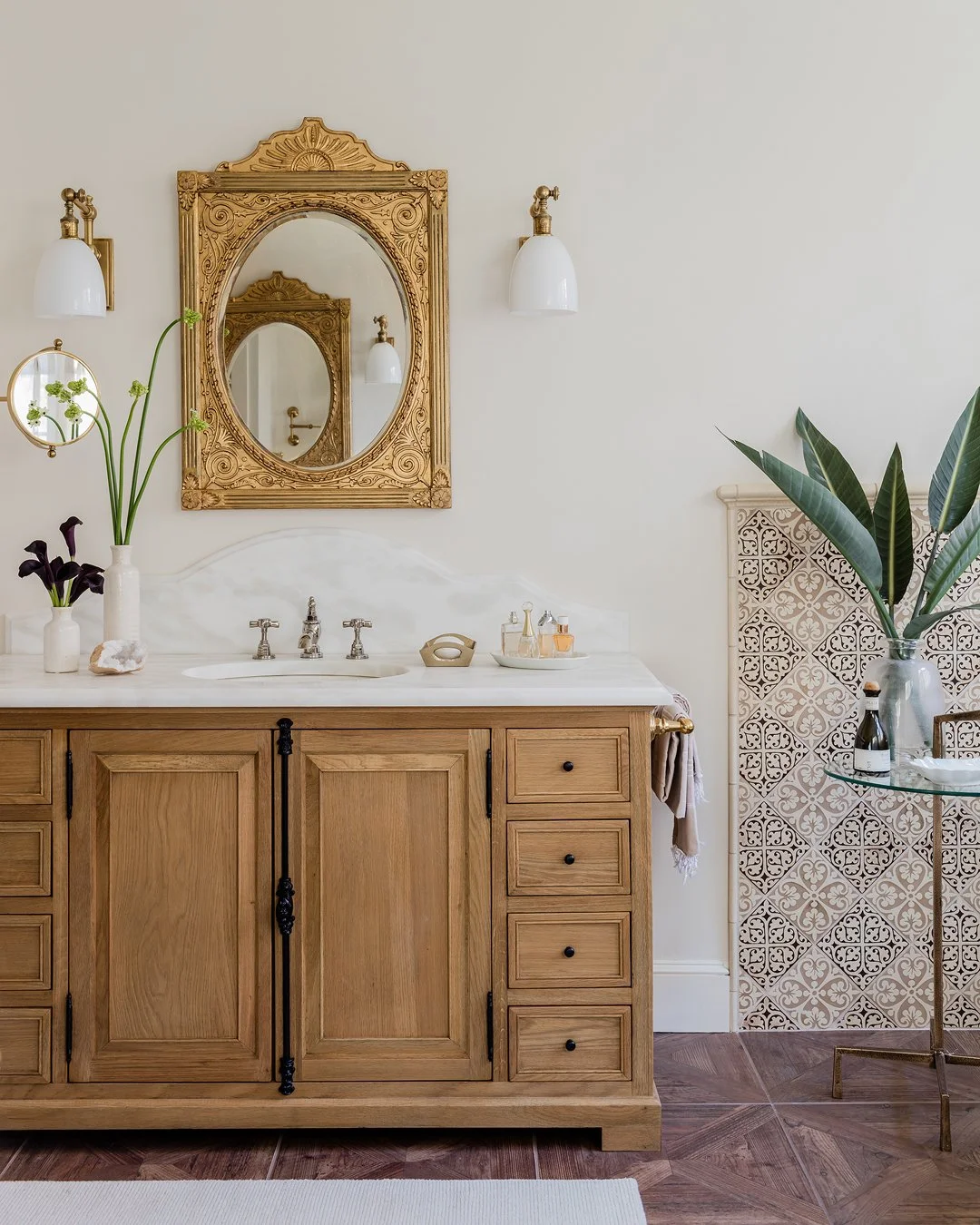 A white oak bathroom vanity with a custom curved marble countertop, decorative patterned tiles and gilded antique mirror