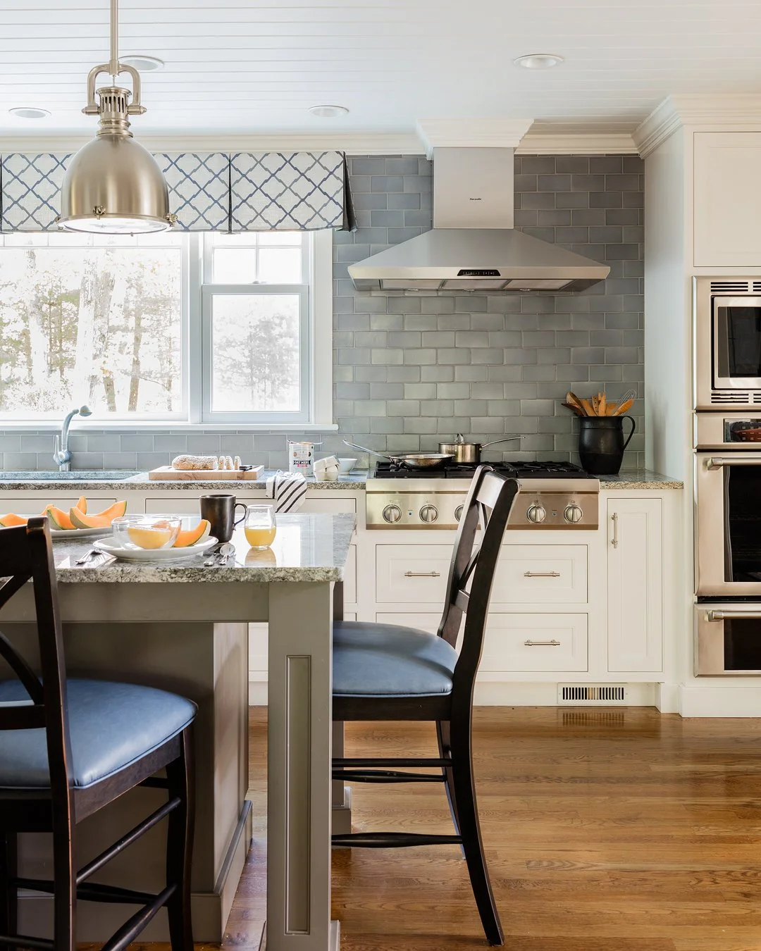 Kitchen detail with white shaker cabinetry, gray blue subway tile backsplash, Thermador range, and patterned roman shade — full service kitchen interior design by Sacris Design, serving MA, New Hampshire and Maine
