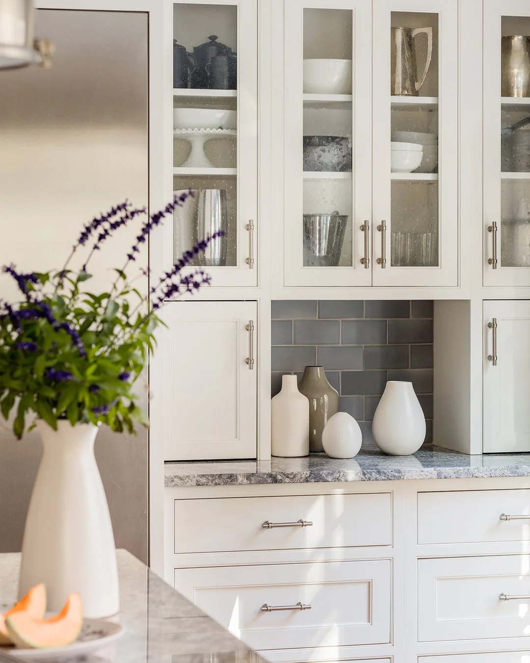 Kitchen cabinetry detail with warm white shaker cabinets, seeded glass doors, granite countertop, and gray blue subway tile — bespoke kitchen design in Merrimack Valley MA by Sacris Design