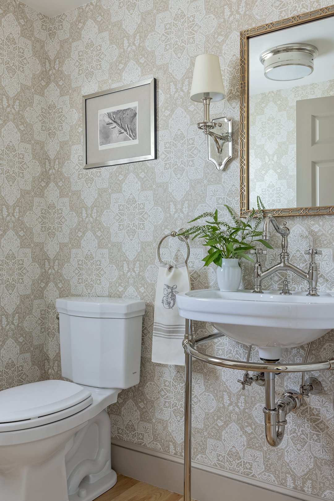 A powder room with patterned Thibaut wallpaper and a vintage-style console sink with traditional polished nickel fixtures