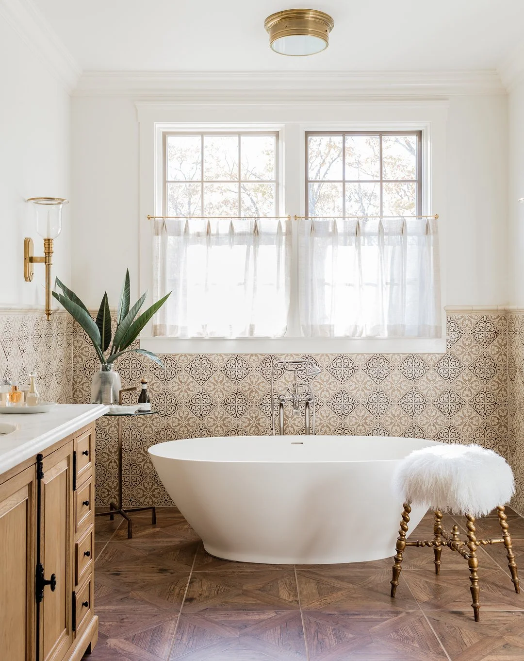 Luxury primary bathroom with freestanding soaking tub, encaustic patterned tile surround, herringbone wood-look tile floor, and brass fixtures — full service interior architecture on the North Shore of Massachusetts by Sacris Design