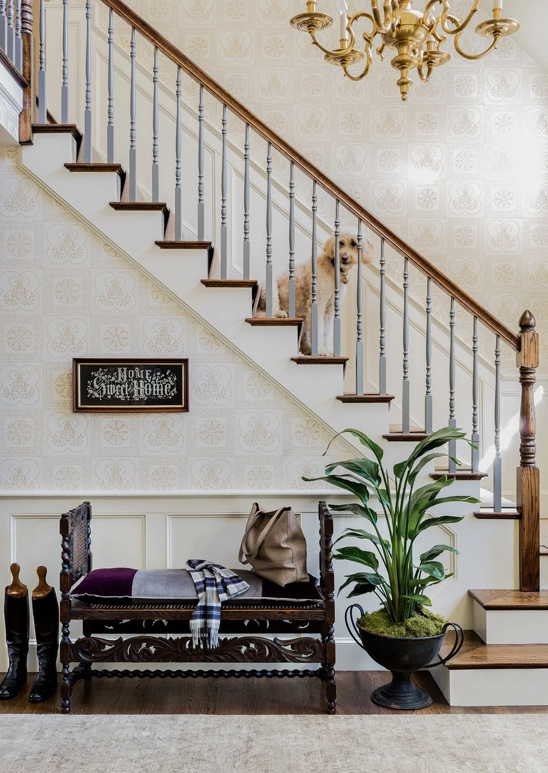 Grand staircase entry hall with decorative tile-pattern wallpaper, carved antique bench, and brass chandelier — luxury historic home interior design on the North Shore of Massachusetts by Sacris Design