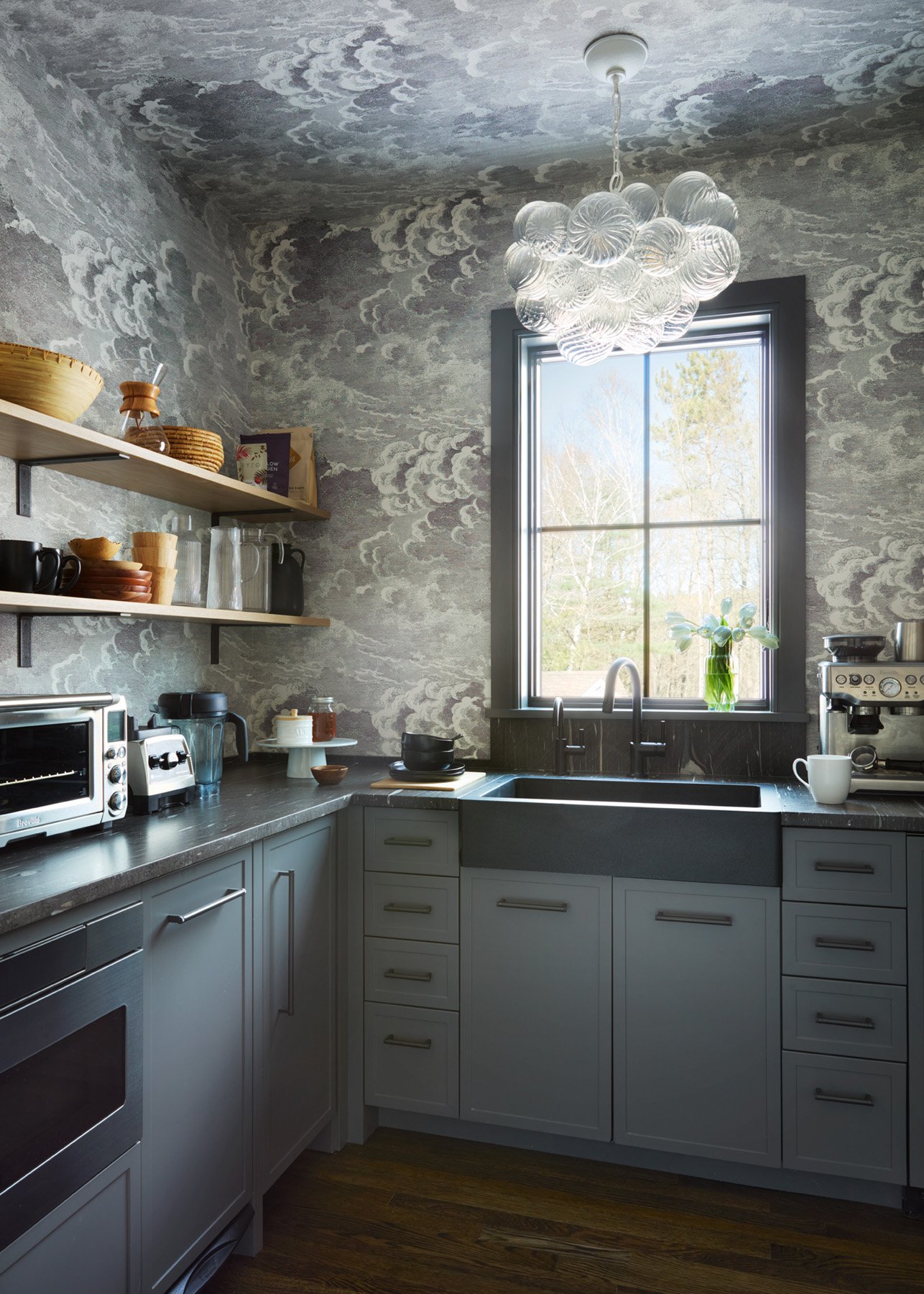 SACRIS working pantry with Fornasetti Nuvolette cloud wallcovering by Cole & Son on walls and ceiling, gray-blue cabinetry, honed granite counters with integrated sink, open white oak shelving and Visual Comfort Talia semi-flush fixture, North Andove