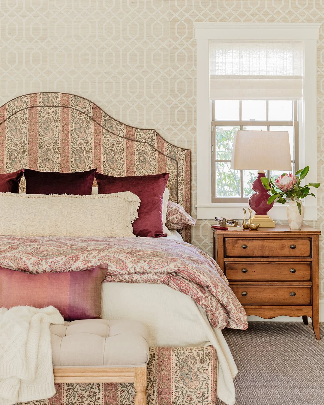 Luxury primary bedroom with custom paisley fabric upholstered headboard, coordinating bedding, and trellis grasscloth wallpaper — full service bedroom design on the North Shore of Massachusetts by Sacris Design