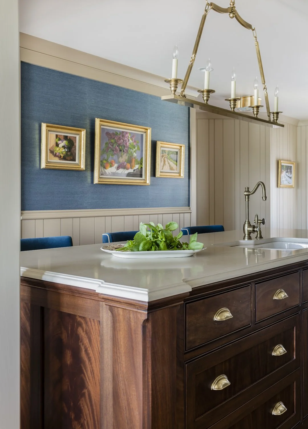 Kitchen island detail with crotch mahogany cabinetry, antique brass cup pulls, brass faucet, and blue grasscloth accent wall with oil painting gallery — bespoke kitchen millwork in Essex County MA by SACRIS
