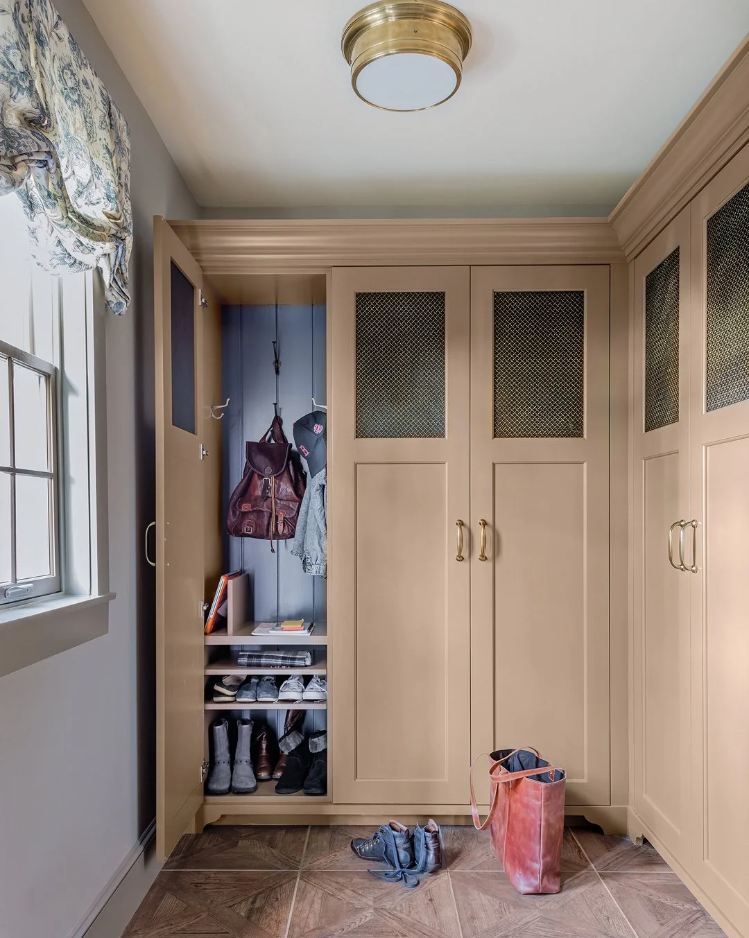 Luxury mudroom with custom painted built-in lockers, brass mesh cabinet inserts, and herringbone tile floor — full service interior architecture on the North Shore of Massachusetts by Sacris Design