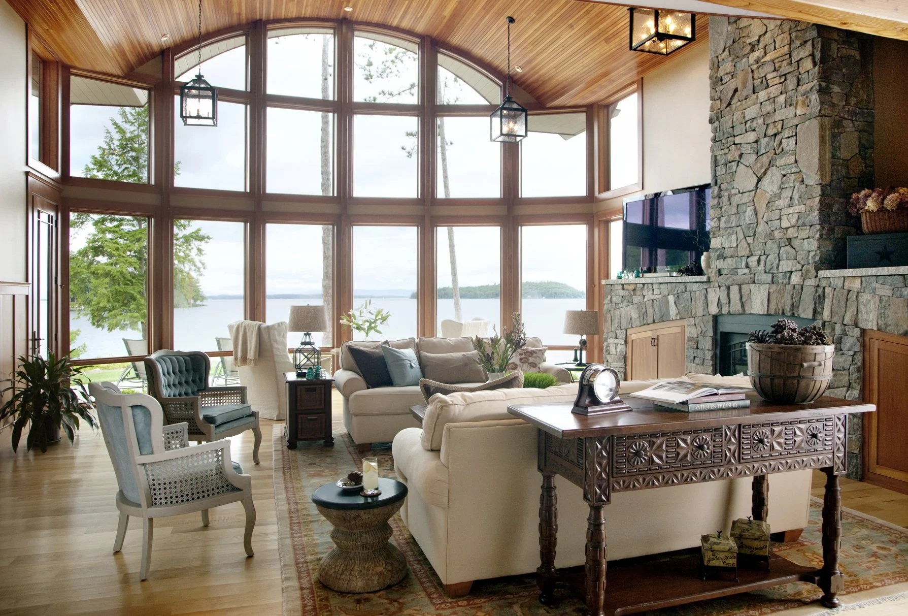 Craftsman lake house great room with barrel vault cedar ceiling, floor-to-ceiling windows with Lake Winnipesaukee views, and stacked stone fireplace — luxury lake house interior design in the Lakes Region of New Hampshire by SACRIS Interior Architect