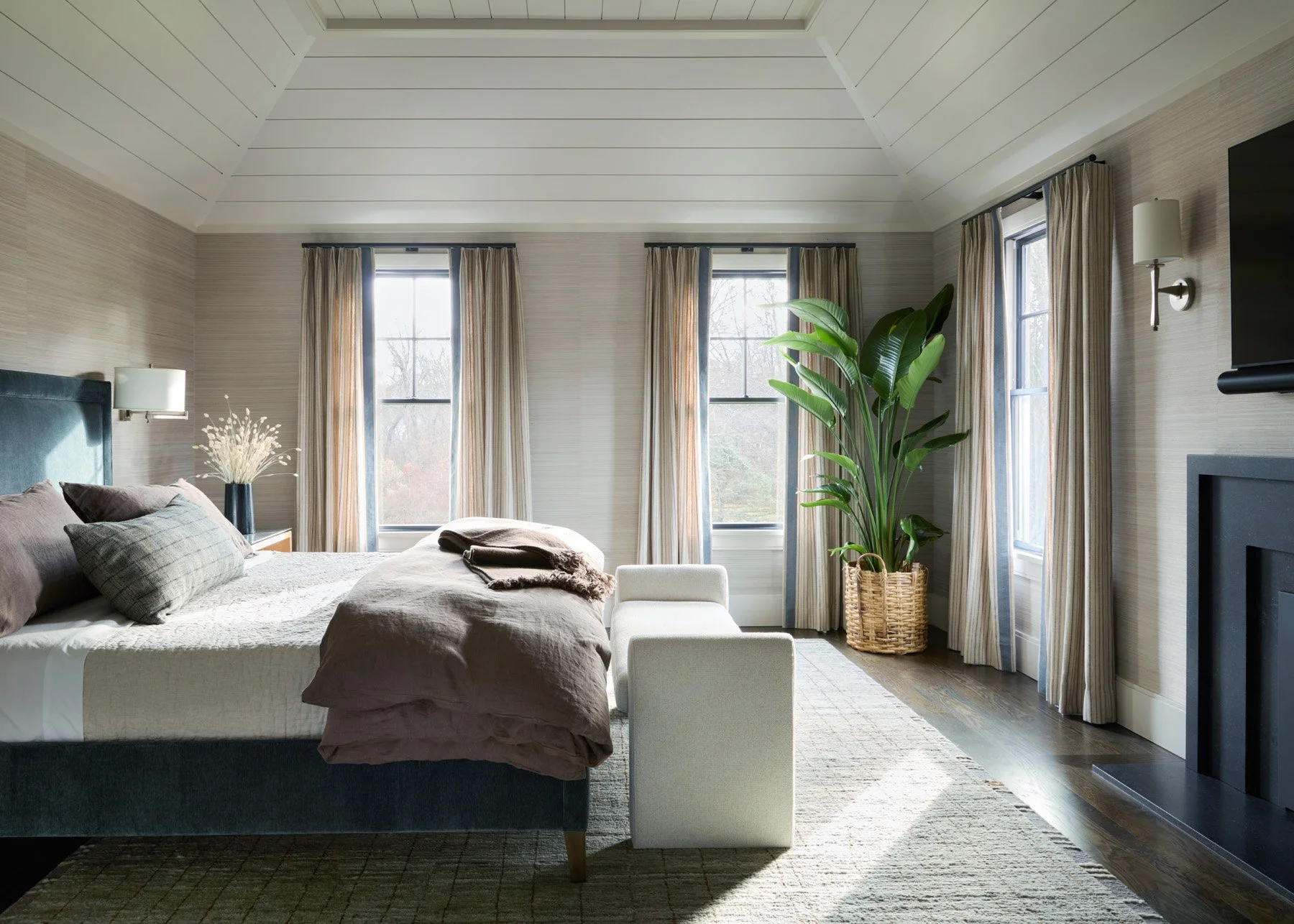 SACRIS primary bedroom with vaulted shiplap ceiling, Thibaut grasscloth wallcovering, Wesley Hall upholstered bed and banded striped drapery, North Andover Massachusetts