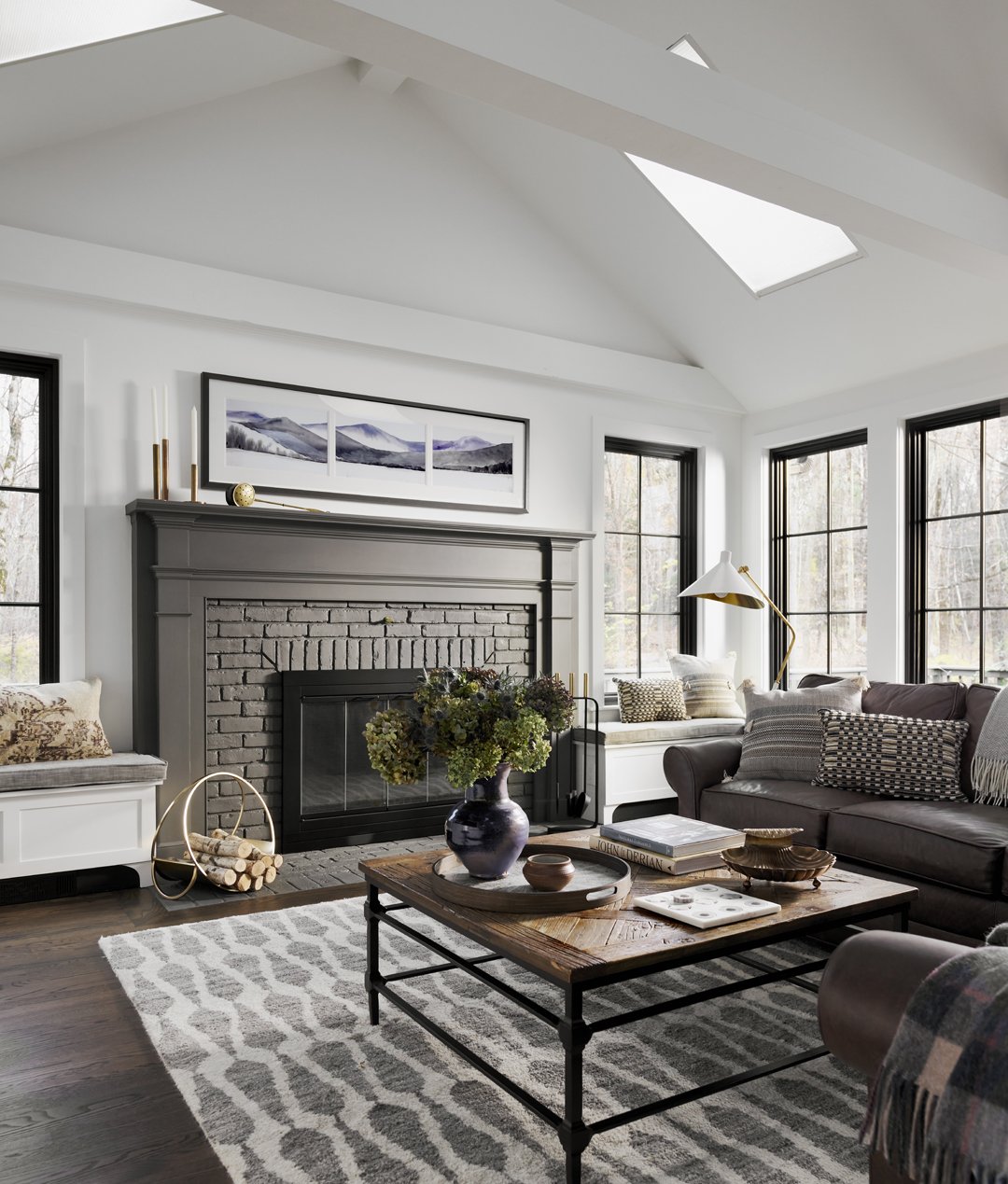 Modern Farmhouse living room with vaulted ceiling with skylights, black window frames, a gray painted brick fireplace, and a wooden coffee table.
