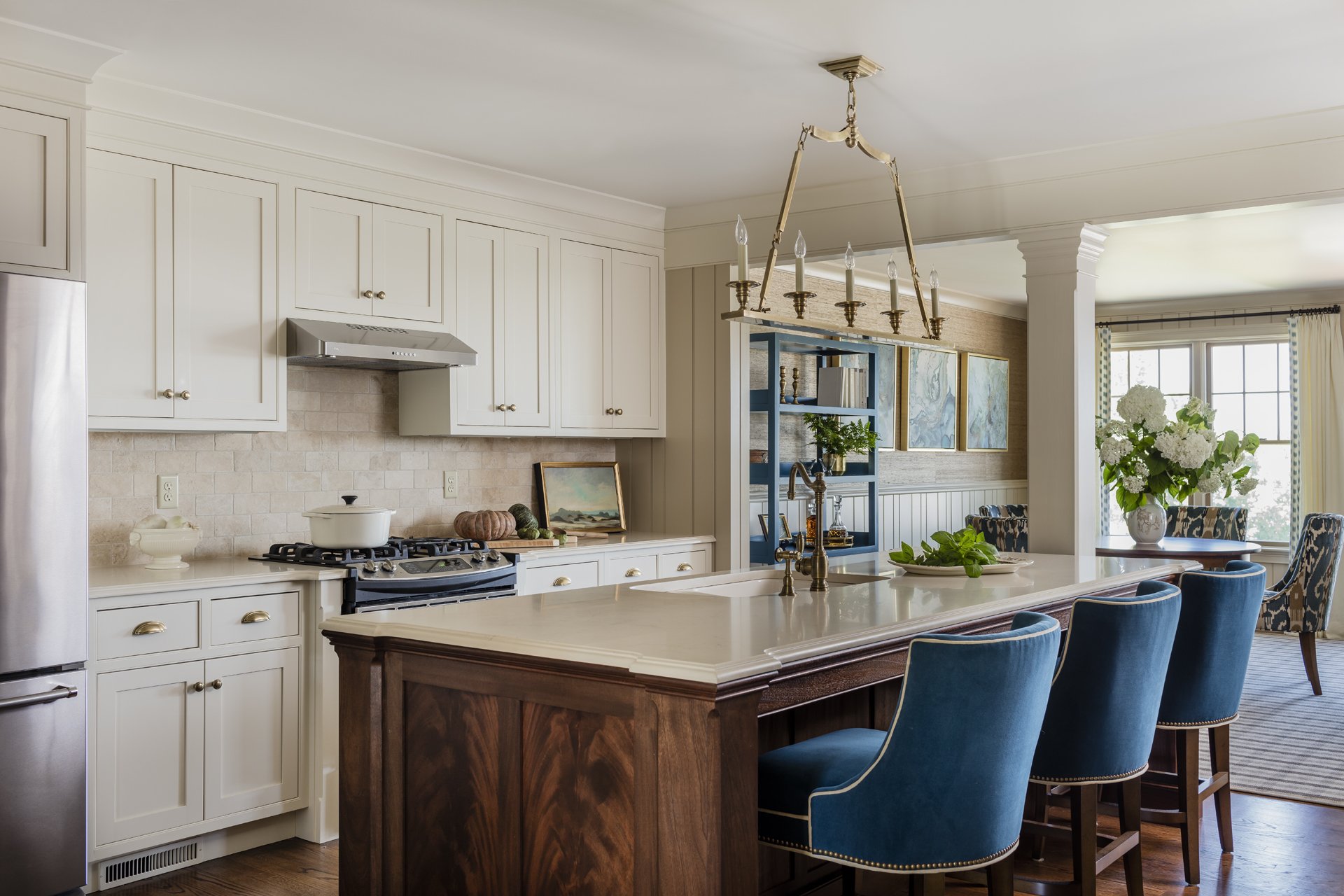 Luxury open plan kitchen with shaker inset cabinetry, crotch mahogany custom island, blue velvet barstools, and brass chandelier with view to dining and living room — full service interior design in Essex County MA by Sacris Design