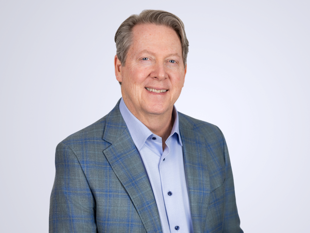 A professional portrait of Roger Pricer. He is wearing a blue shirt and a blue and gray tartan suitcoat.