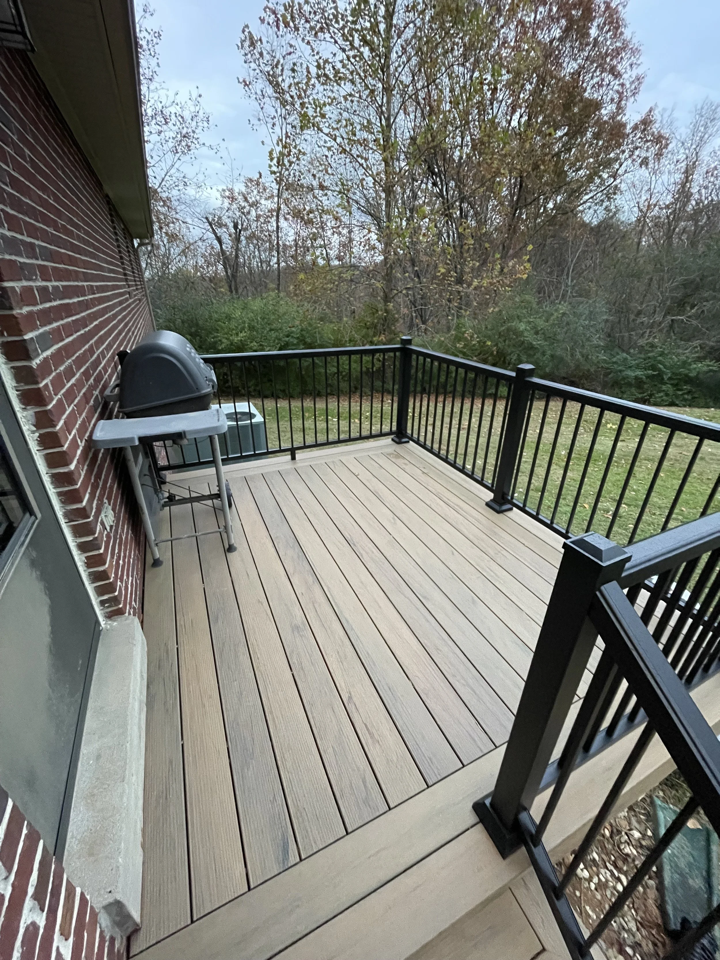 Check out this affordable long lasting composite deck professionally constructed with black metal aluminum railings, a grilling station, and a great view of the outdoors. Composite decking is a great long term low maintenance decision.