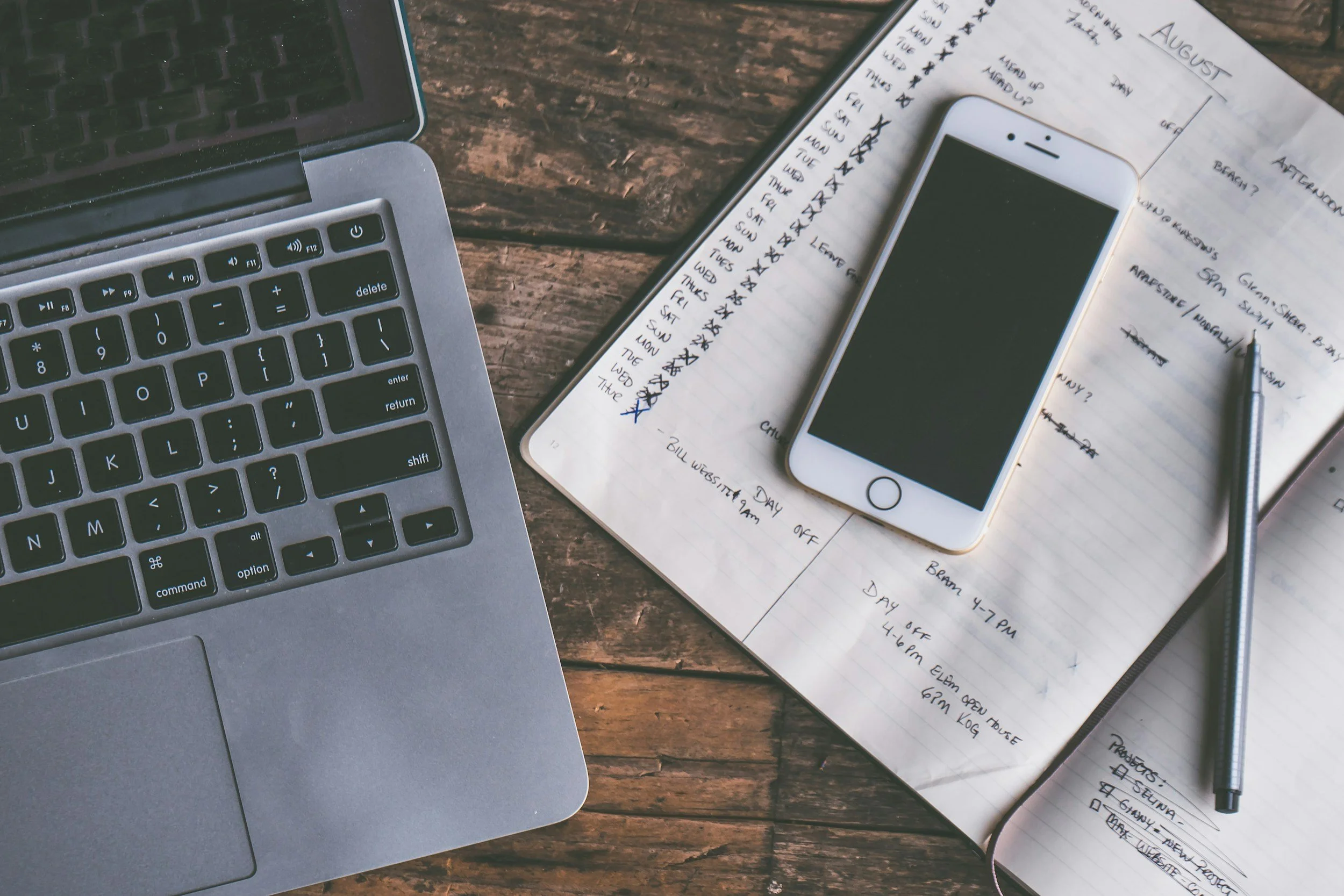 An image of an open laptop, a phone, and a notebook.