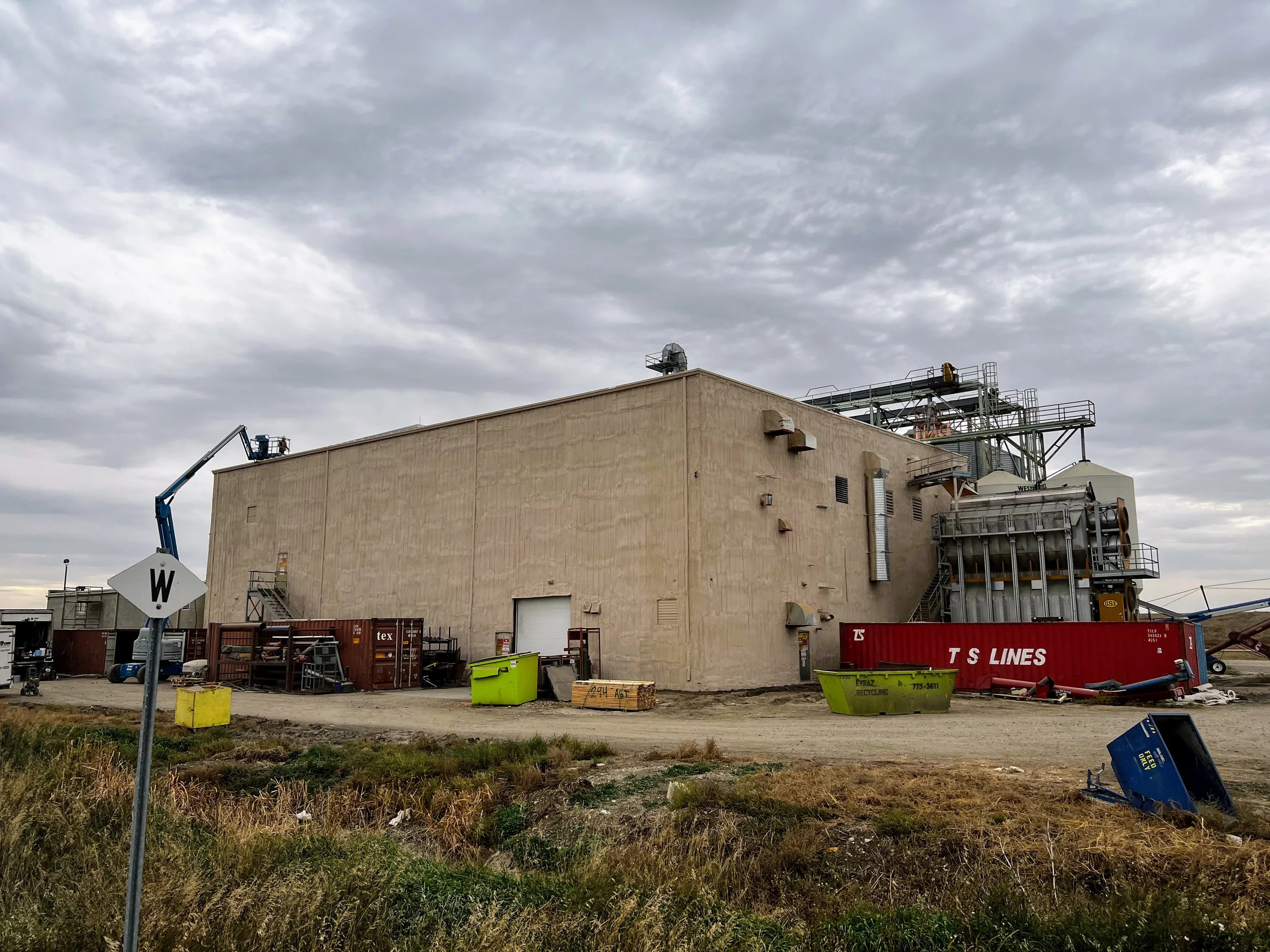 Industrial building with construction equipment, storage containers, and overcast sky.