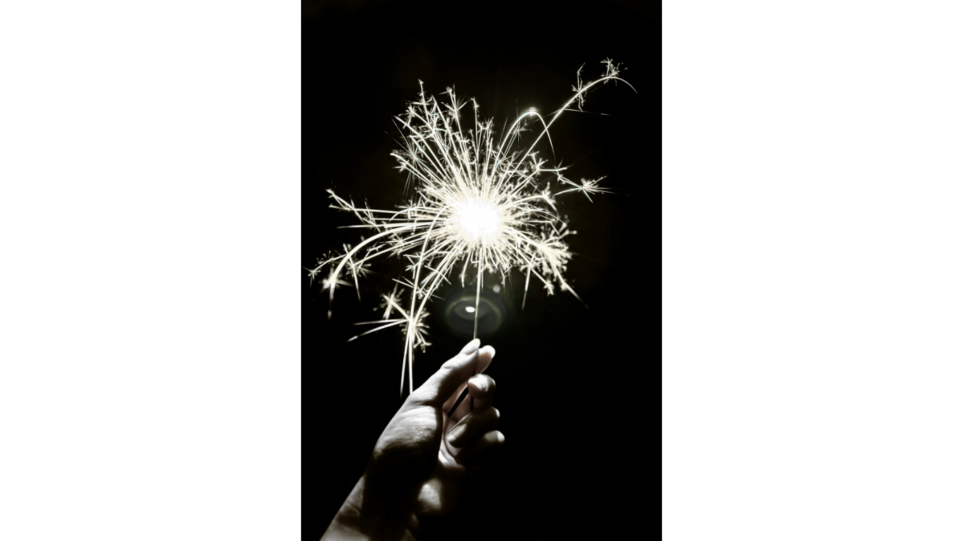 Person holding a lit sparkler against a dark background.