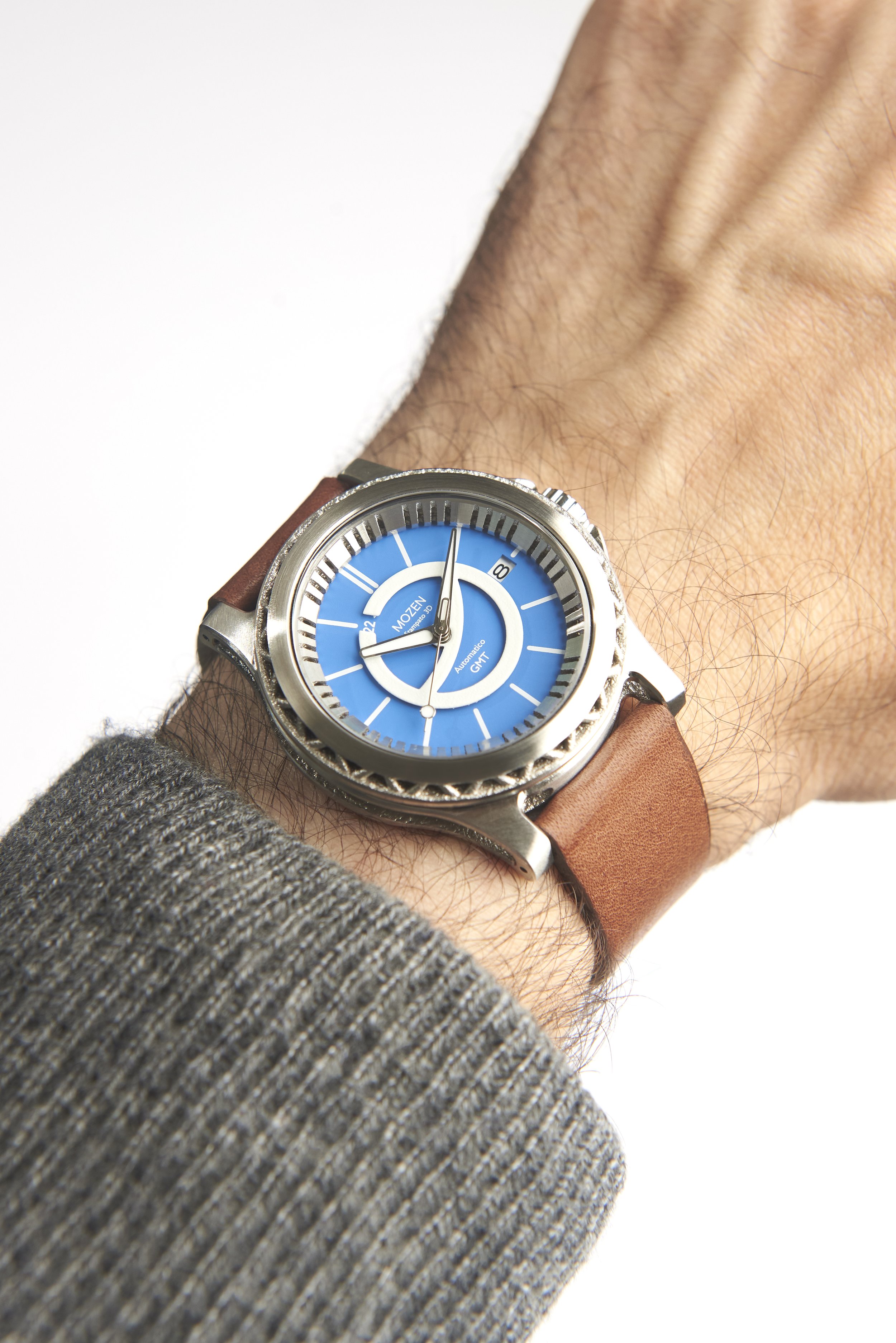 A wristwatch with a bright blue dial, silver case, and brown leather strap worn over a gray textured sleeve.