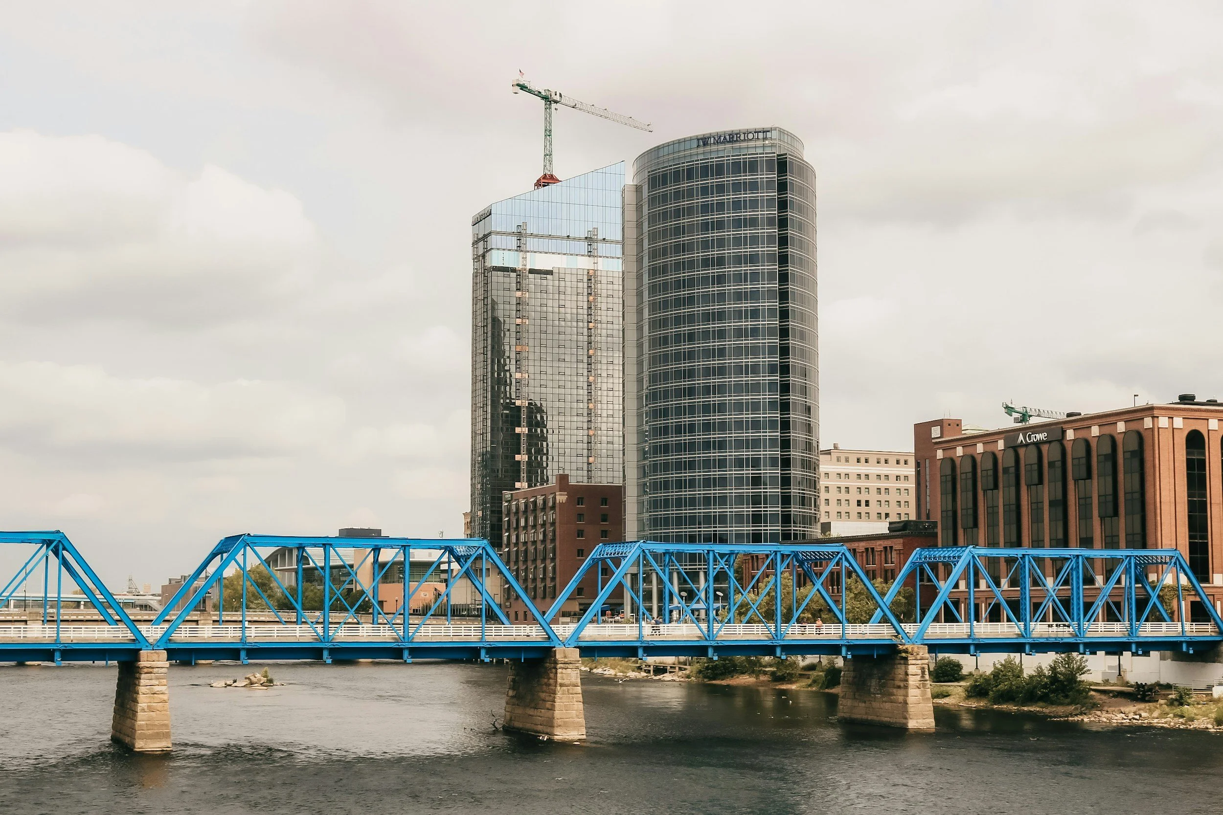 Cityscape view of modern buildings with a blue bridge crossing a river in the foreground.