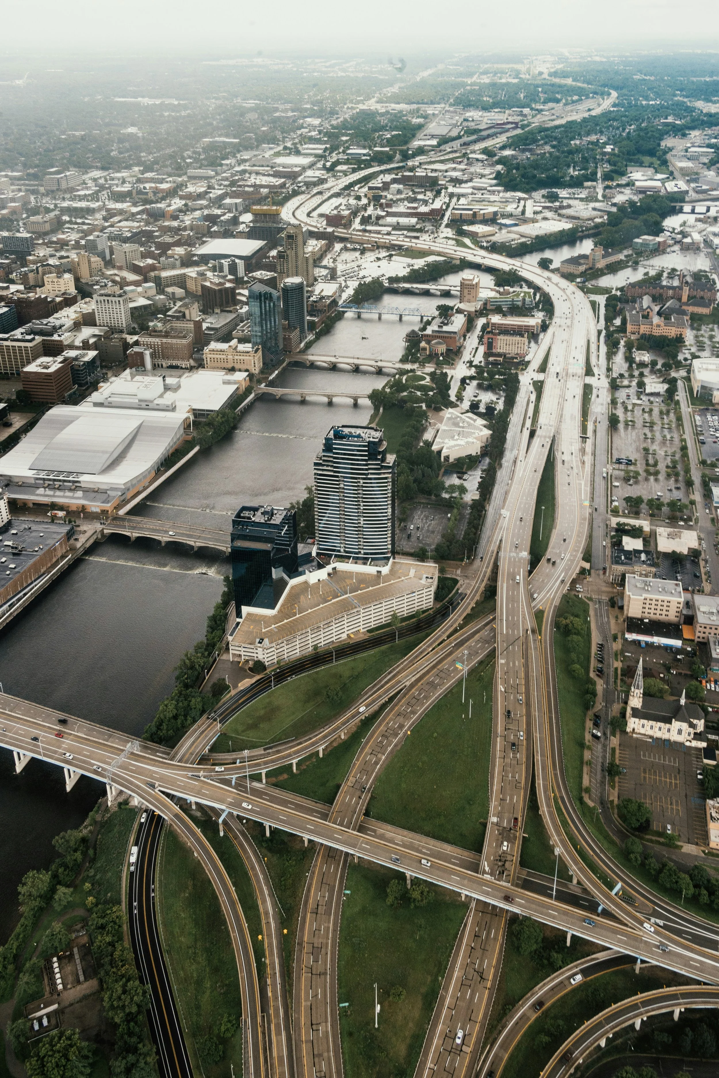 Aerial view of a city with multiple highways, bridges over water, tall buildings, and an overcast sky.