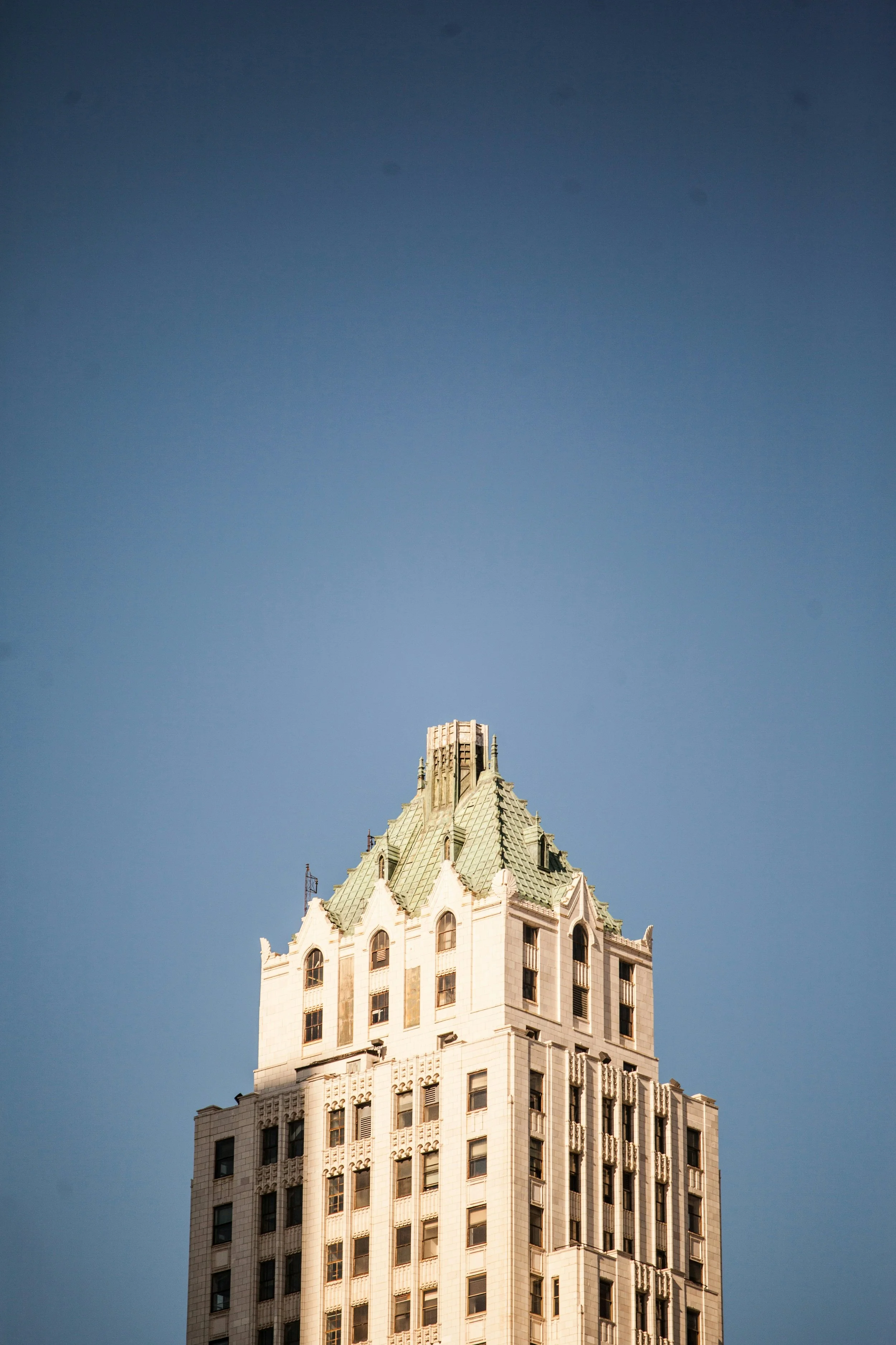 Tall building with a ornate, green-tiled roof against a clear blue sky.