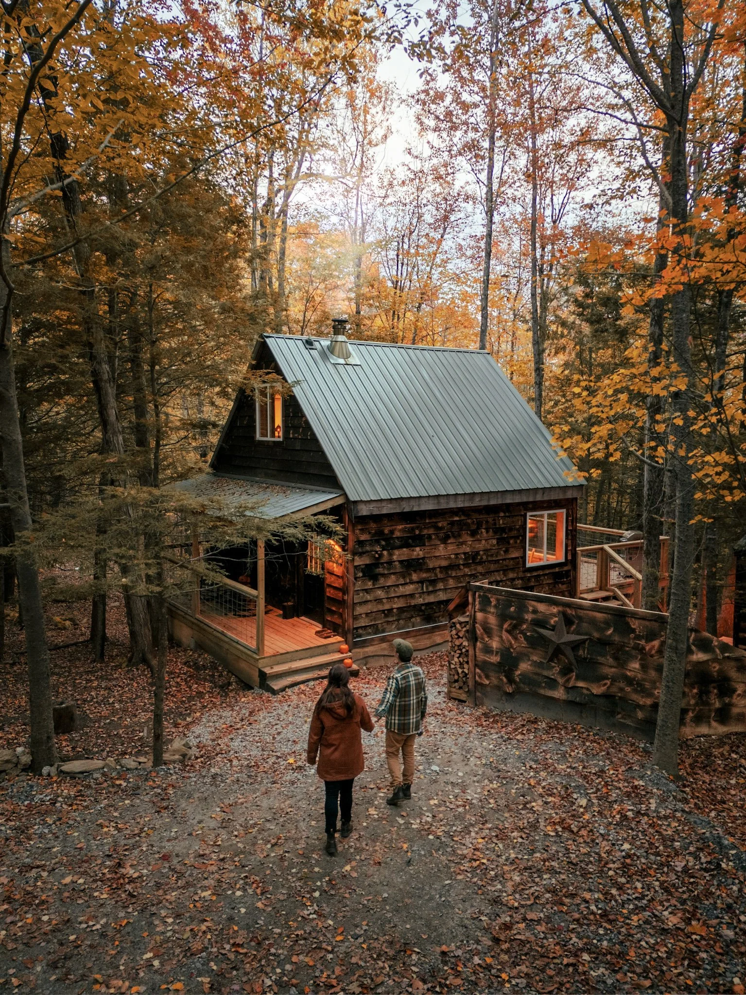 A couple walks towards a rustic cabin in an autumn forest during sunset.