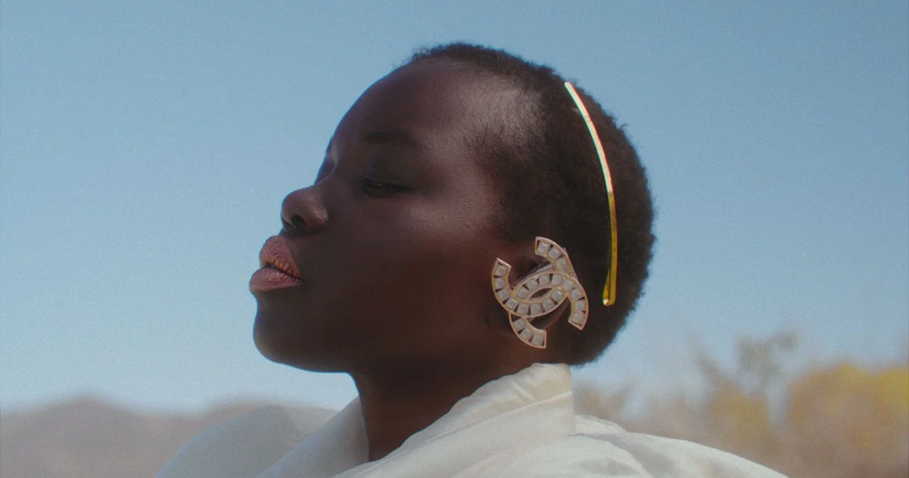 Close-up of a woman with short hair wearing large, decorative earrings with a landscape background.
