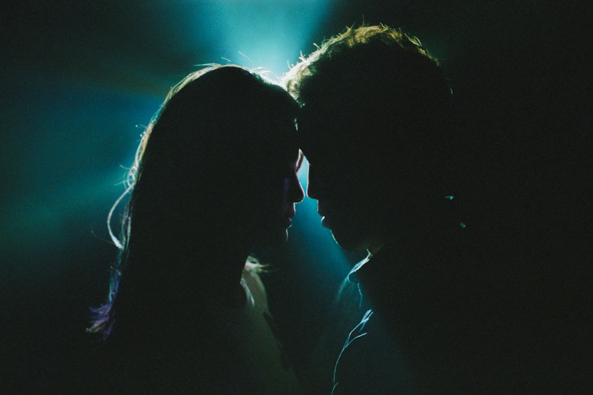 Silhouette of a couple facing each other with foreheads touching, backlit with a soft glow around their heads, creating a romantic and intimate atmosphere.