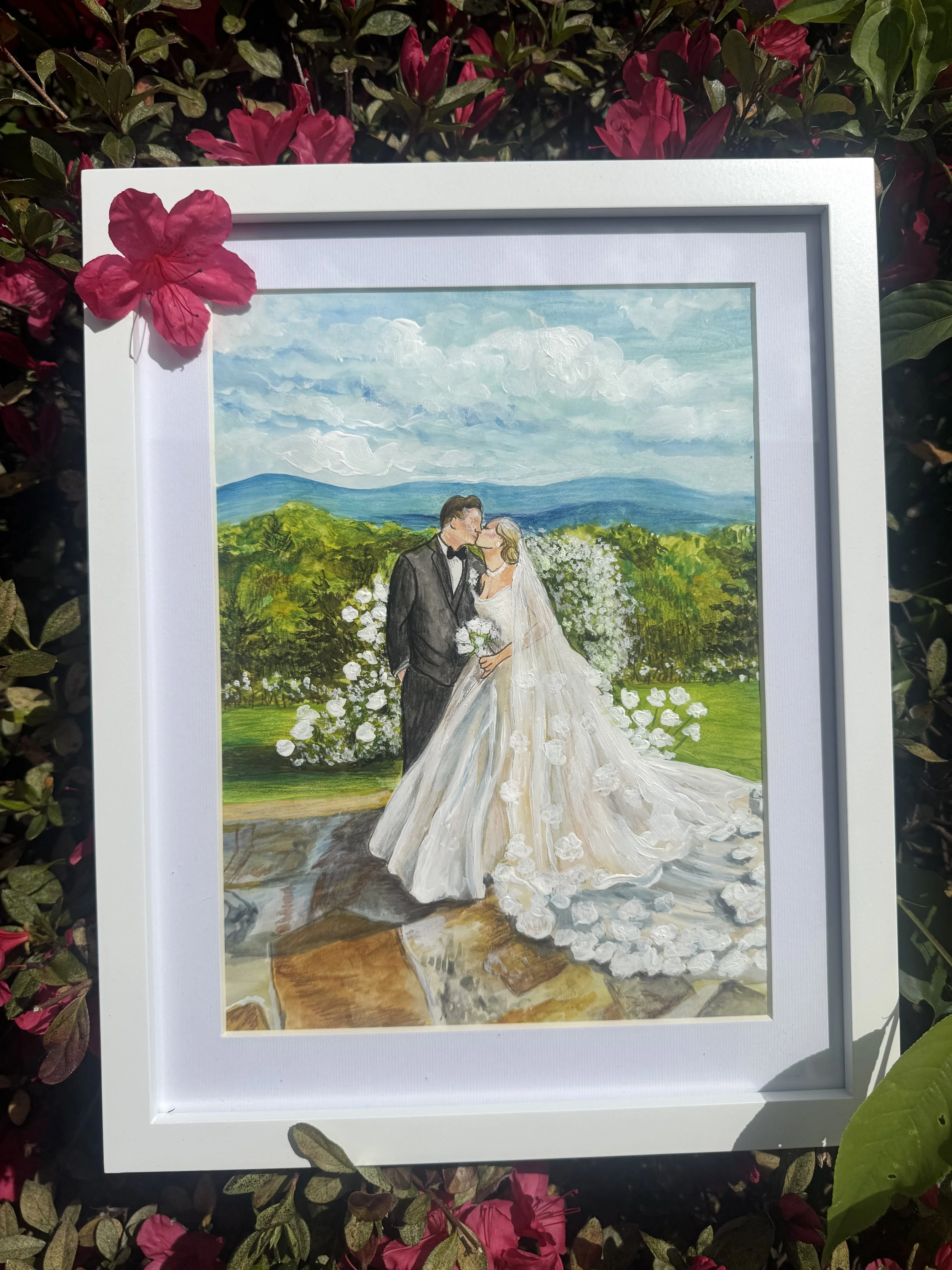 A framed watercolor wedding portrait of a bride and groom kissing in a garden with green foliage and distant mountains in the background, surrounded by pink flowers.