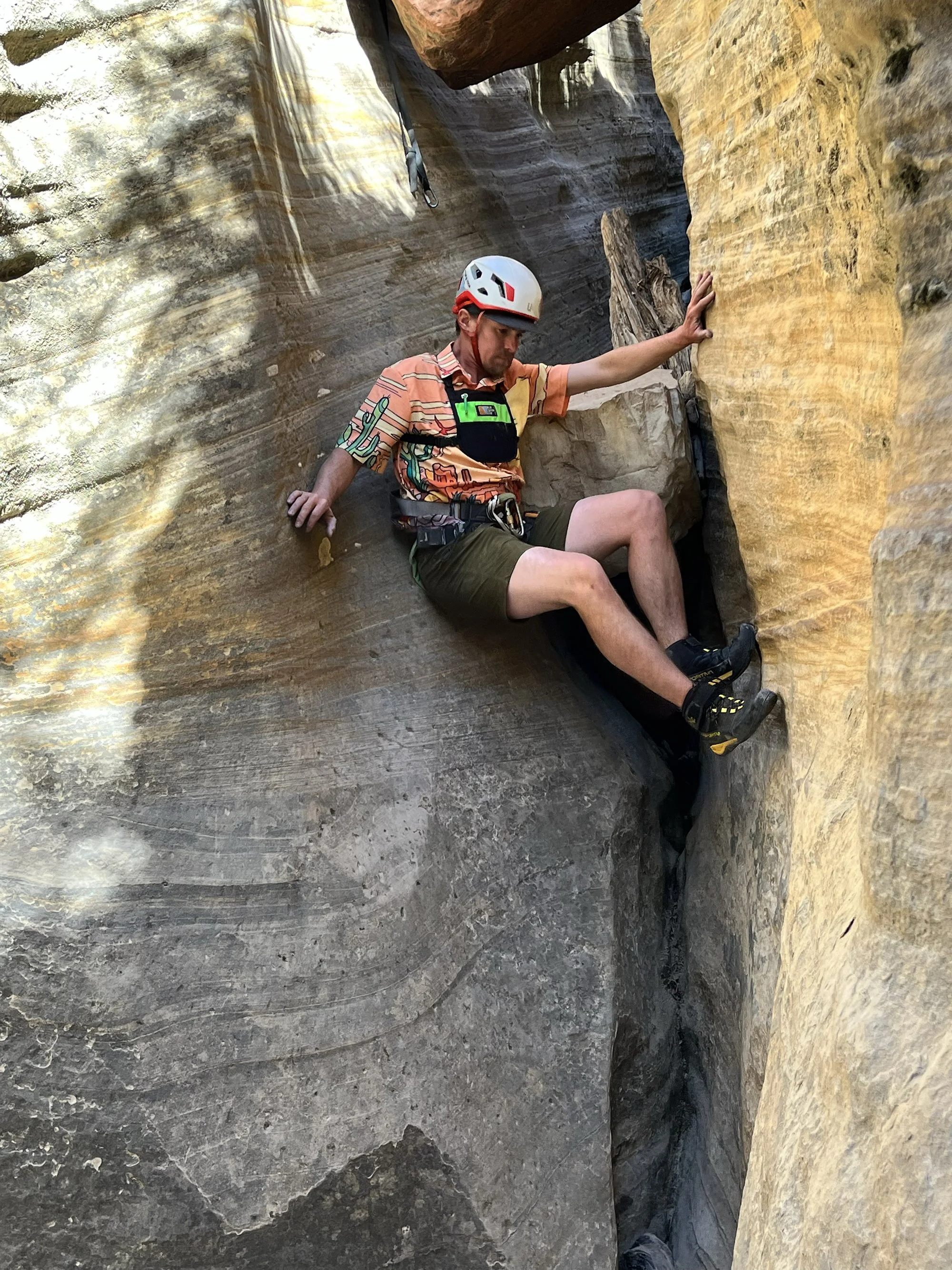 Person rock climbing in a narrow canyon with rock formations.