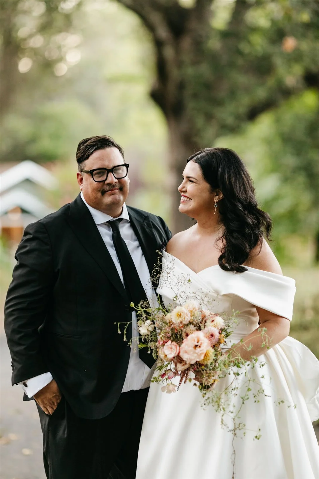 Couple's casual portrait with the bride holding a bouquet of subtle warm-colored roses with a woodland vibe on the grounds of The Madrona -Planned by COJ Events-Palm Springs Destination Wedding