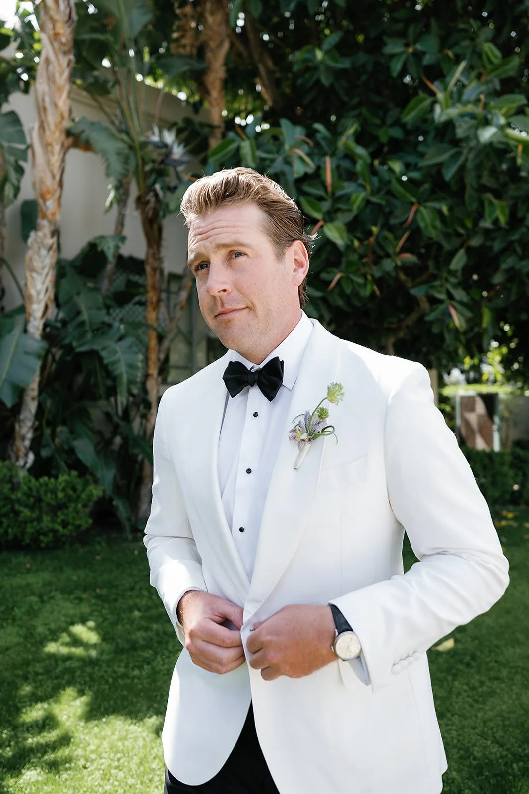 Groom getting dressed at a Merv Griffin Estate wedding with outdoor green garden party decor designed by COJ Events