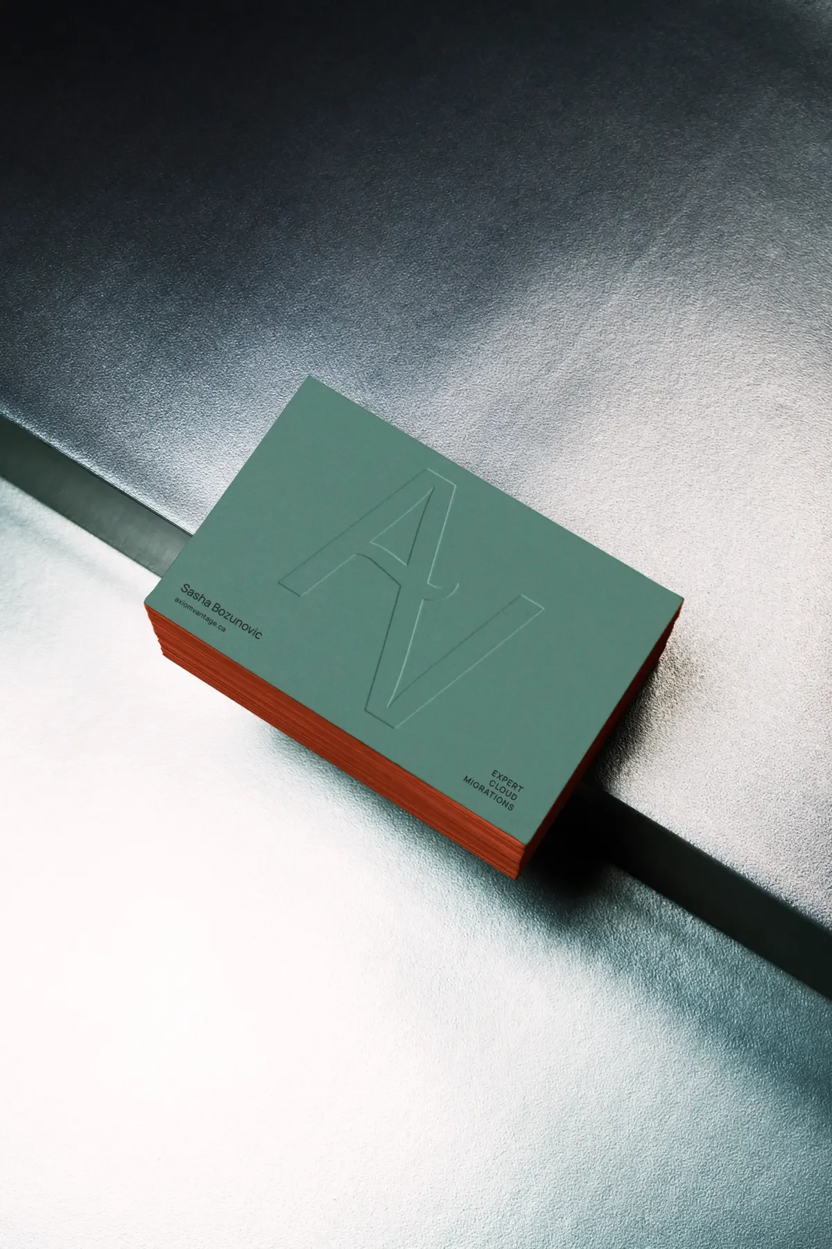Stack of green Axiom Vantage business cards with an embossed AV monogram and orange painted edges