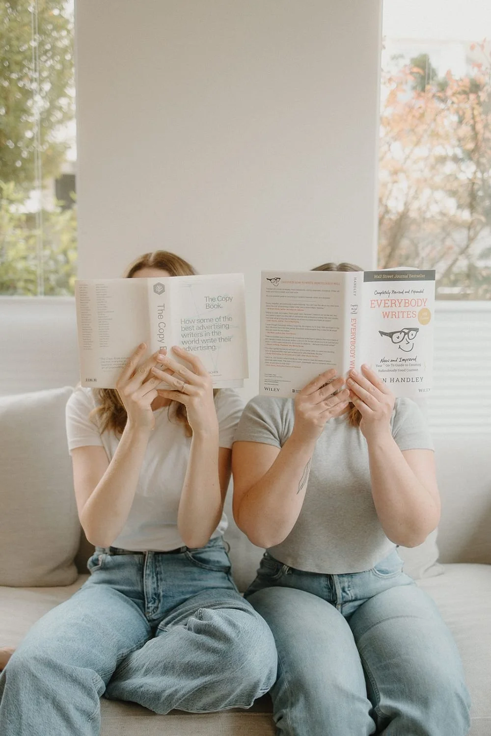Isobel griffin and Samara Bortz from In Tandem Studios sitting on a couch with copywriting books in front of their faces
