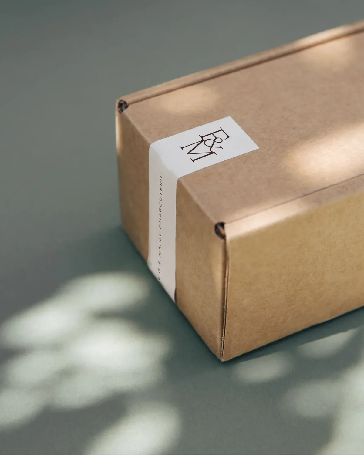 Kraft box sealed with a Fig & Maple Charcuterie monogram label, in dappled sunlight