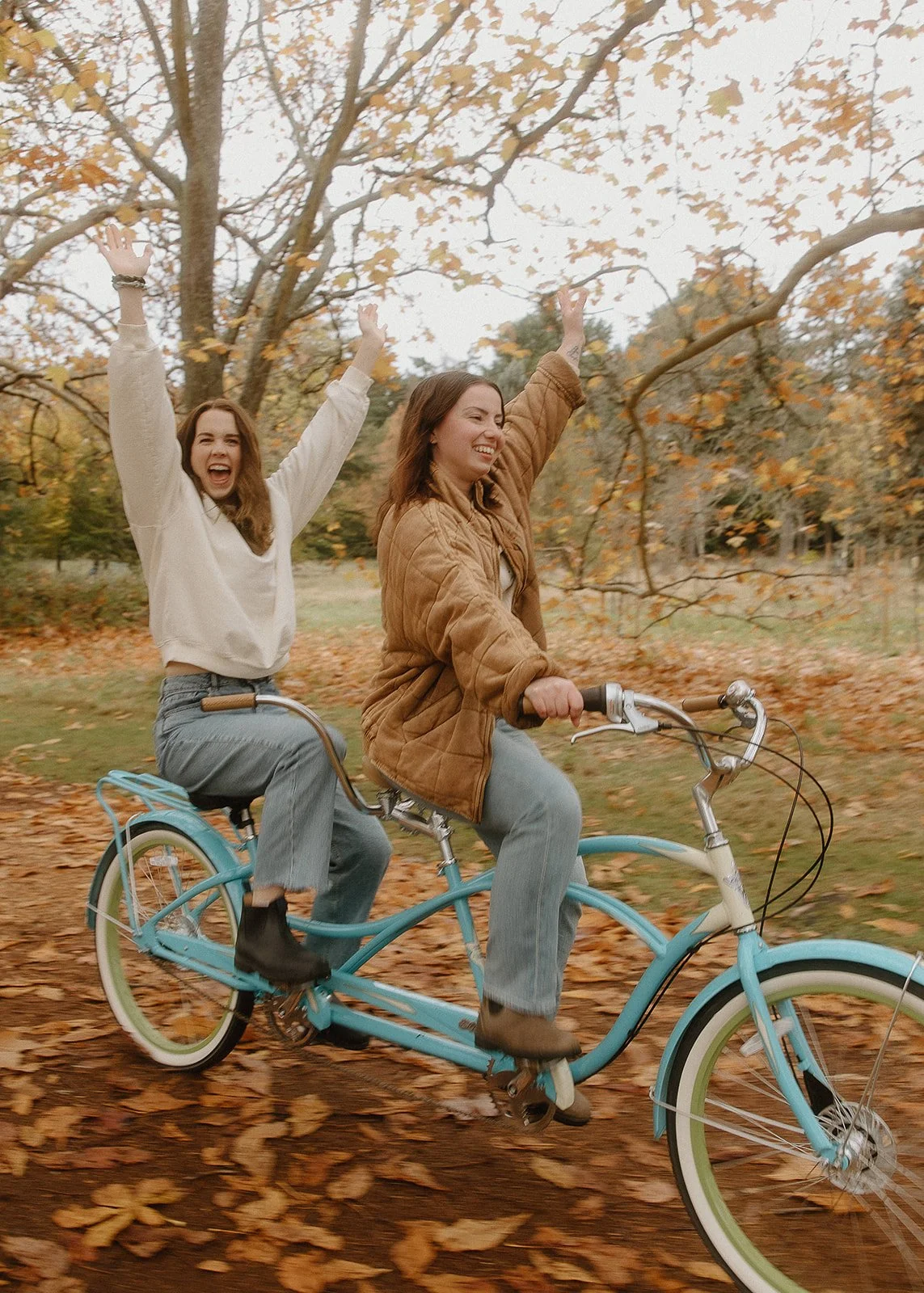 samara and isobel from in tandem studios riding on a teal tandem bicycle through the woods on a fall day