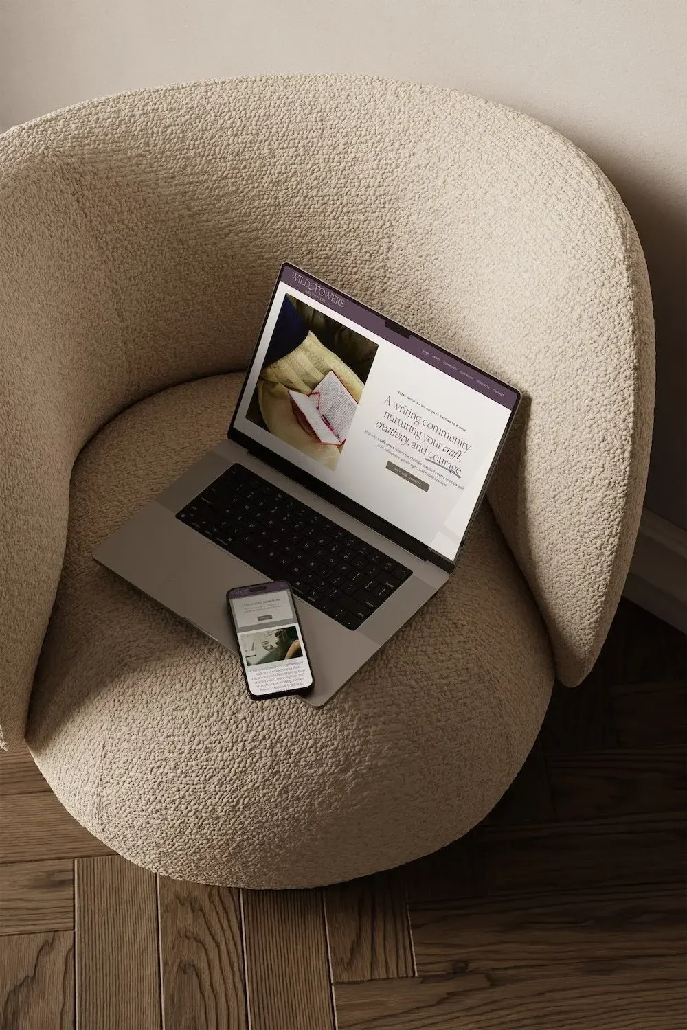 Laptop and phone on a bouclé chair showing the Wildflowers writing community website design